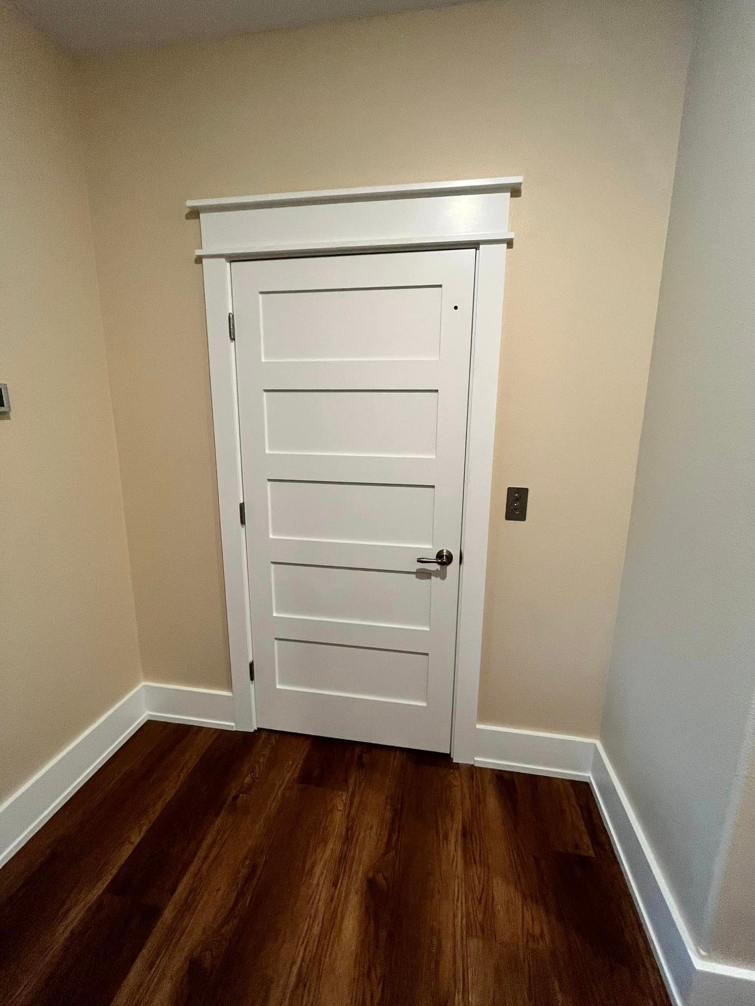 Small room with a white paneled door, gray walls, and dark wood flooring.