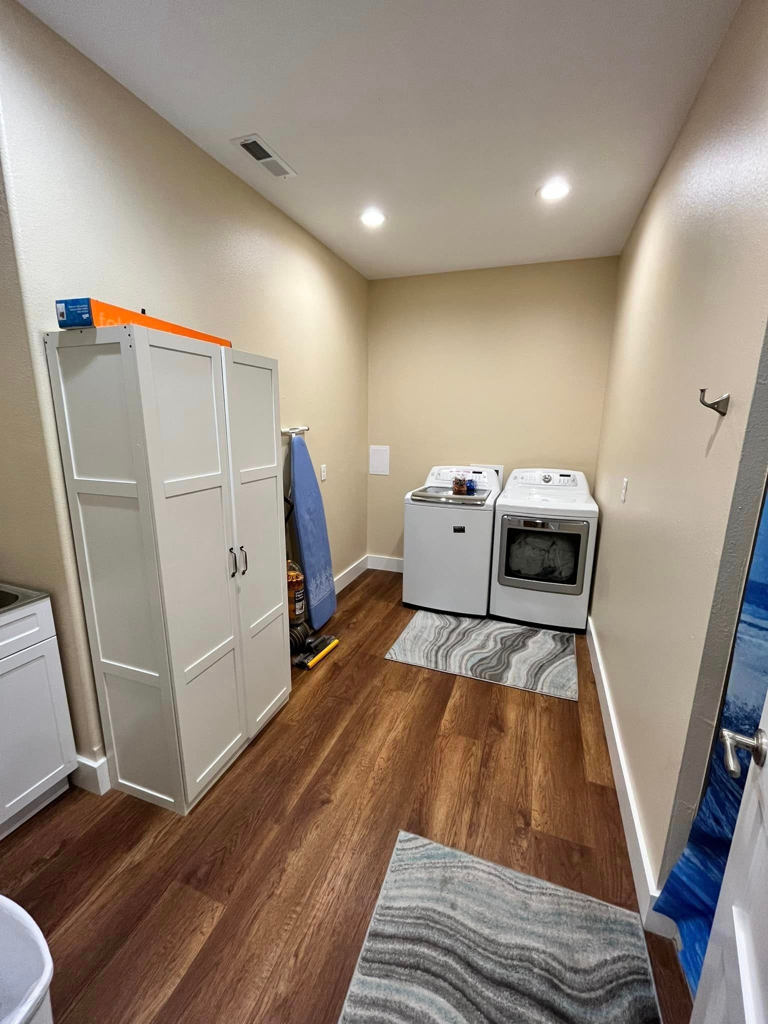 Laundry room with washer and dryer, white cabinets, and a wooden floor with rugs
