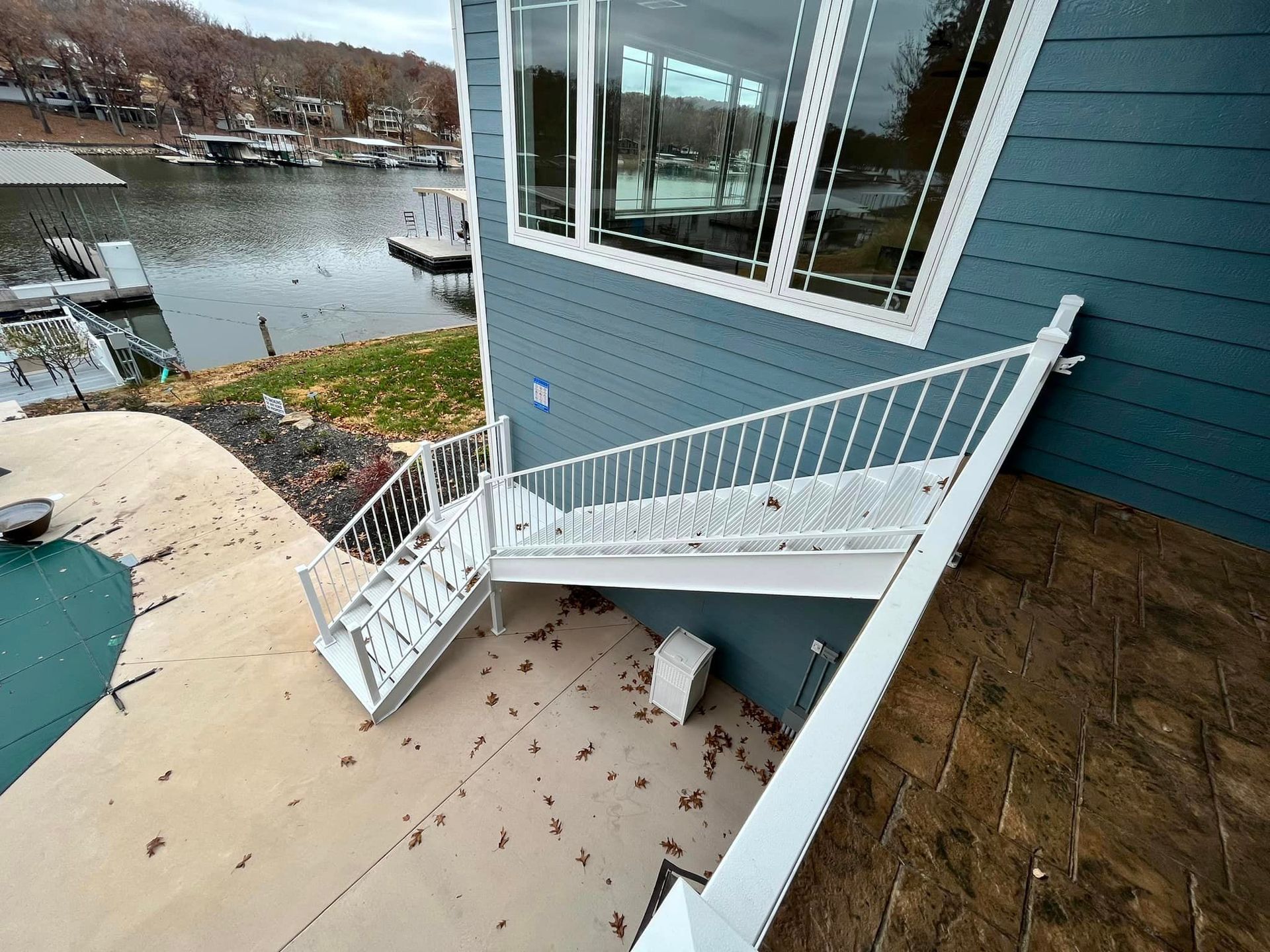 White staircase with railing beside a blue house overlooking a river and yard