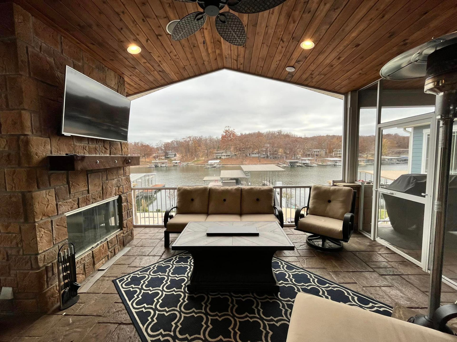 Covered patio with fireplace, TV, seating, and a lake view through large windows