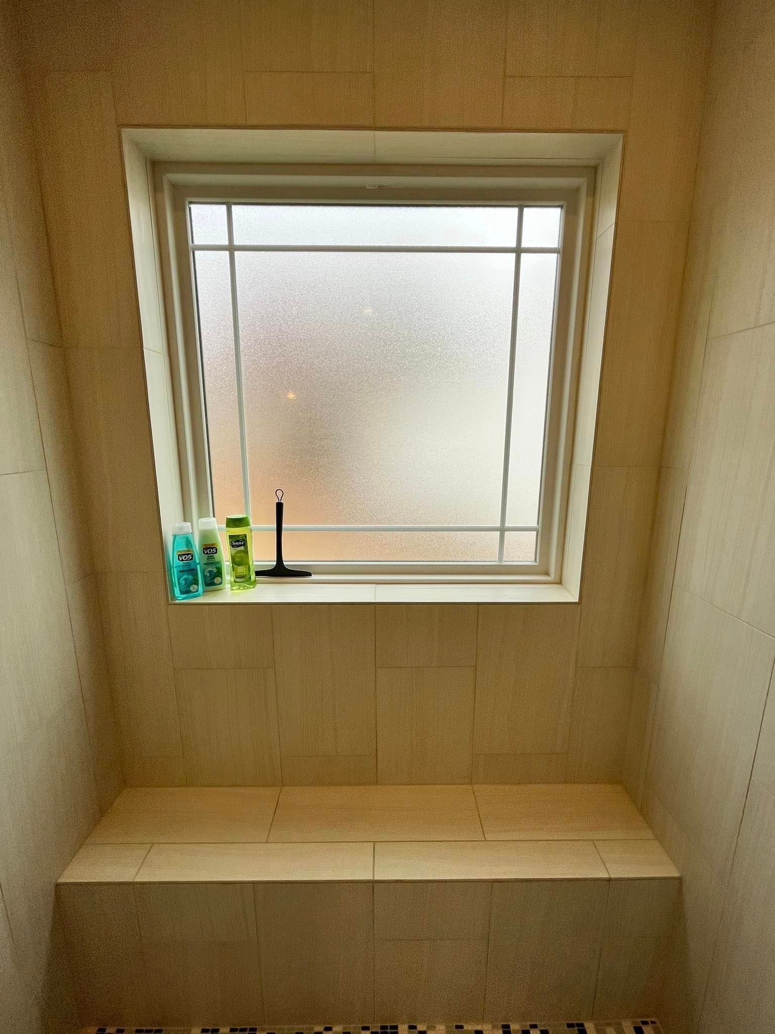 Small bathroom with frosted window, two bottles on the sill, and a tiled bench below.