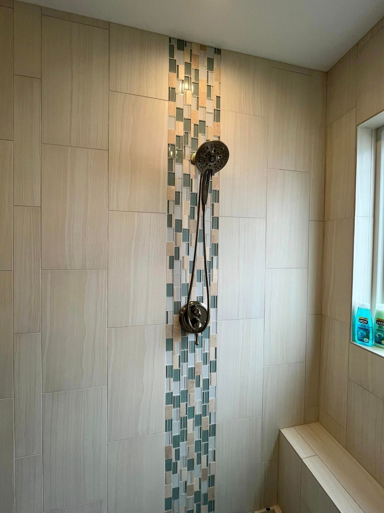 Modern tiled shower wall with two black shower fixtures and a small window on the right.