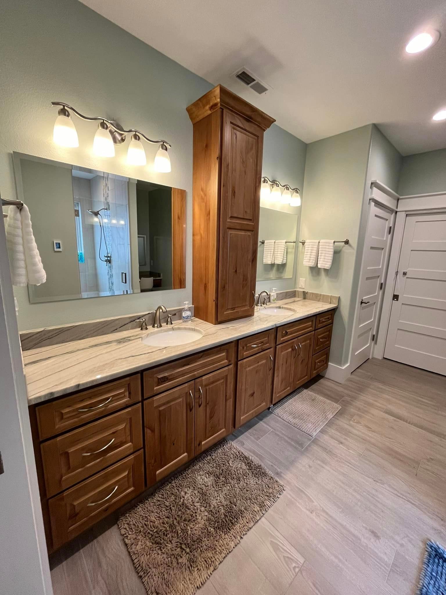 Bathroom vanity with double sinks, large mirror, wood cabinets, and a central tall storage cabinet.