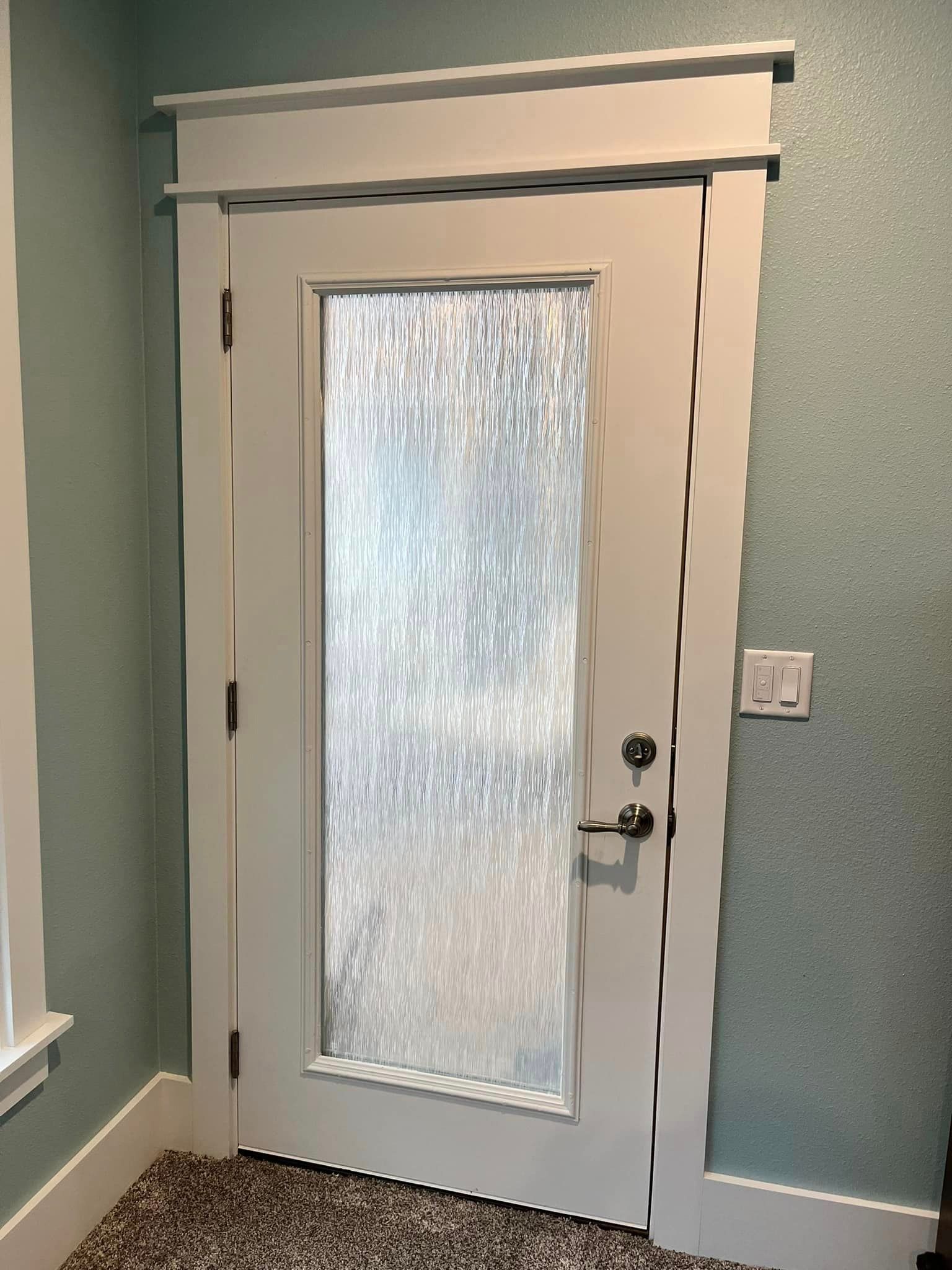 White interior door with frosted glass panel and black handle in a teal hallway