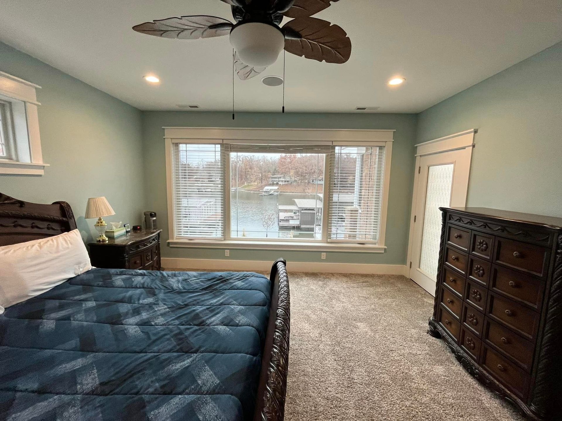 Bedroom with blue bedding, dresser, ceiling fan, and large window overlooking snow outside
