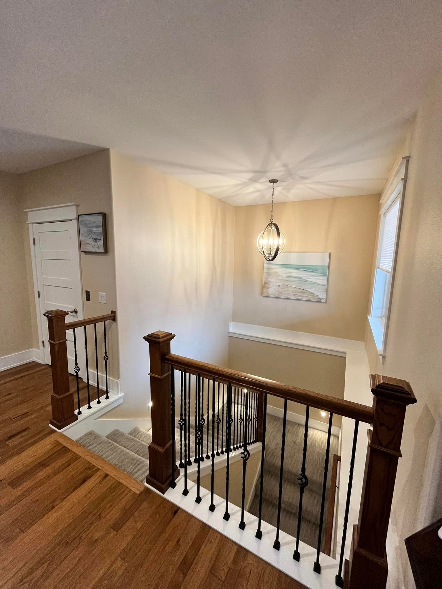 Upstairs hallway with wood floors, white walls, a stair railing, and a hanging light over the stairwell