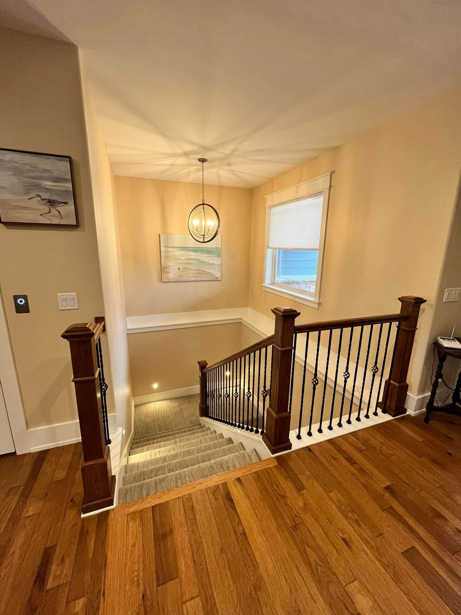 Stair landing with wooden railing, beige walls, hardwood floor, and a hanging light over carpeted stairs.