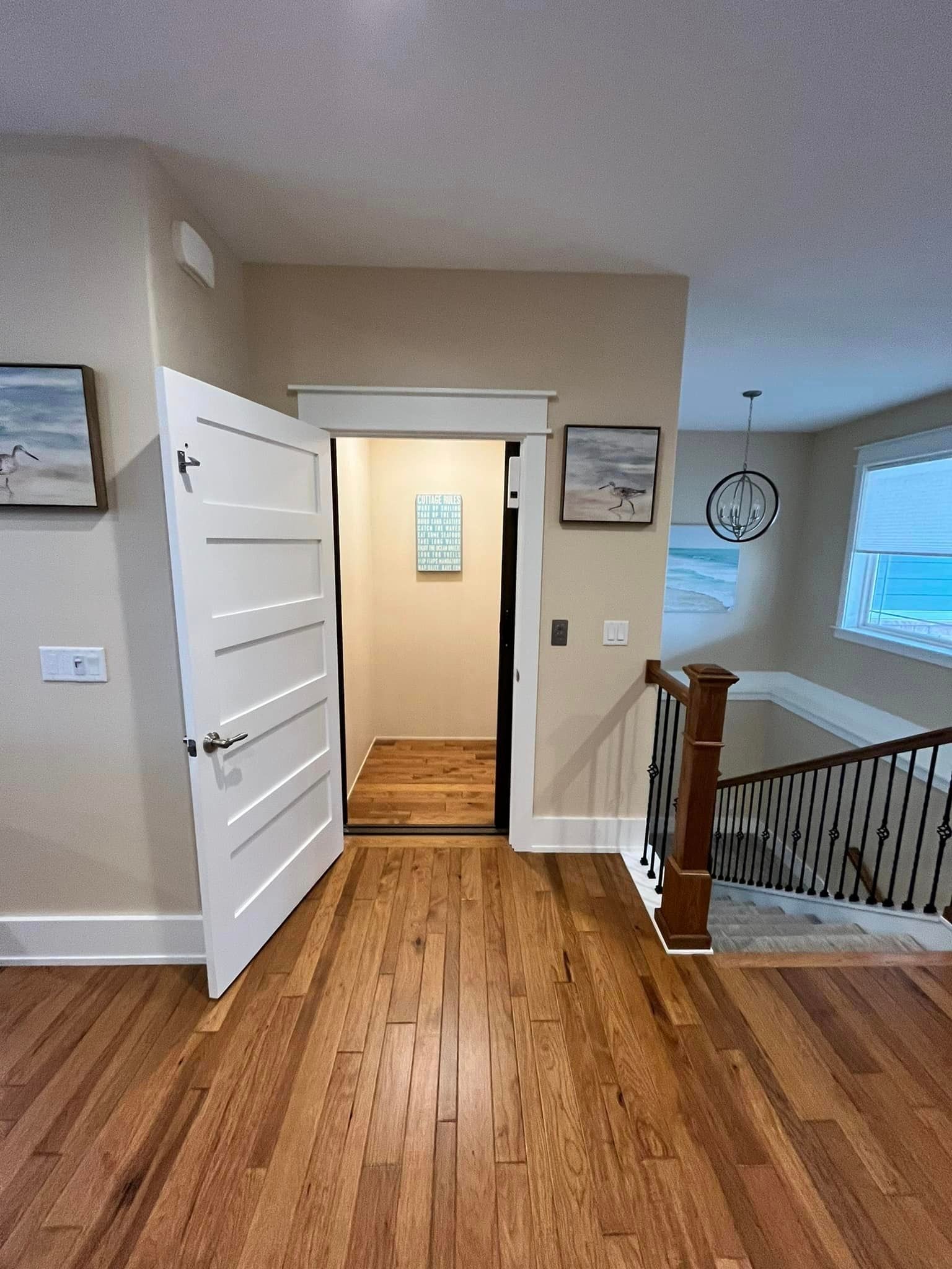 Hallway with hardwood floors, open white door, and a stair railing beside a small upstairs landing