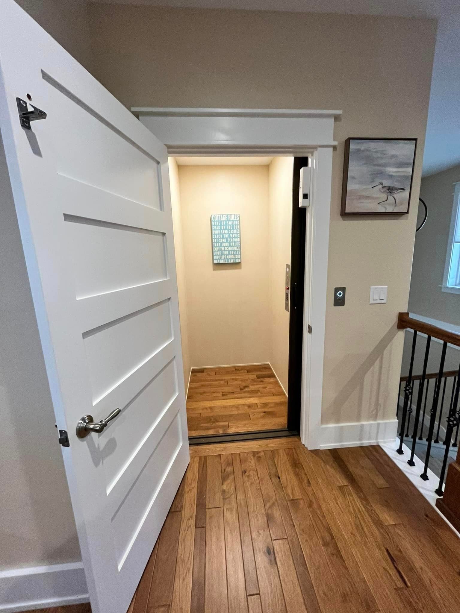 Open white door to a hallway with hardwood floors and beige walls, lit doorway ahead.