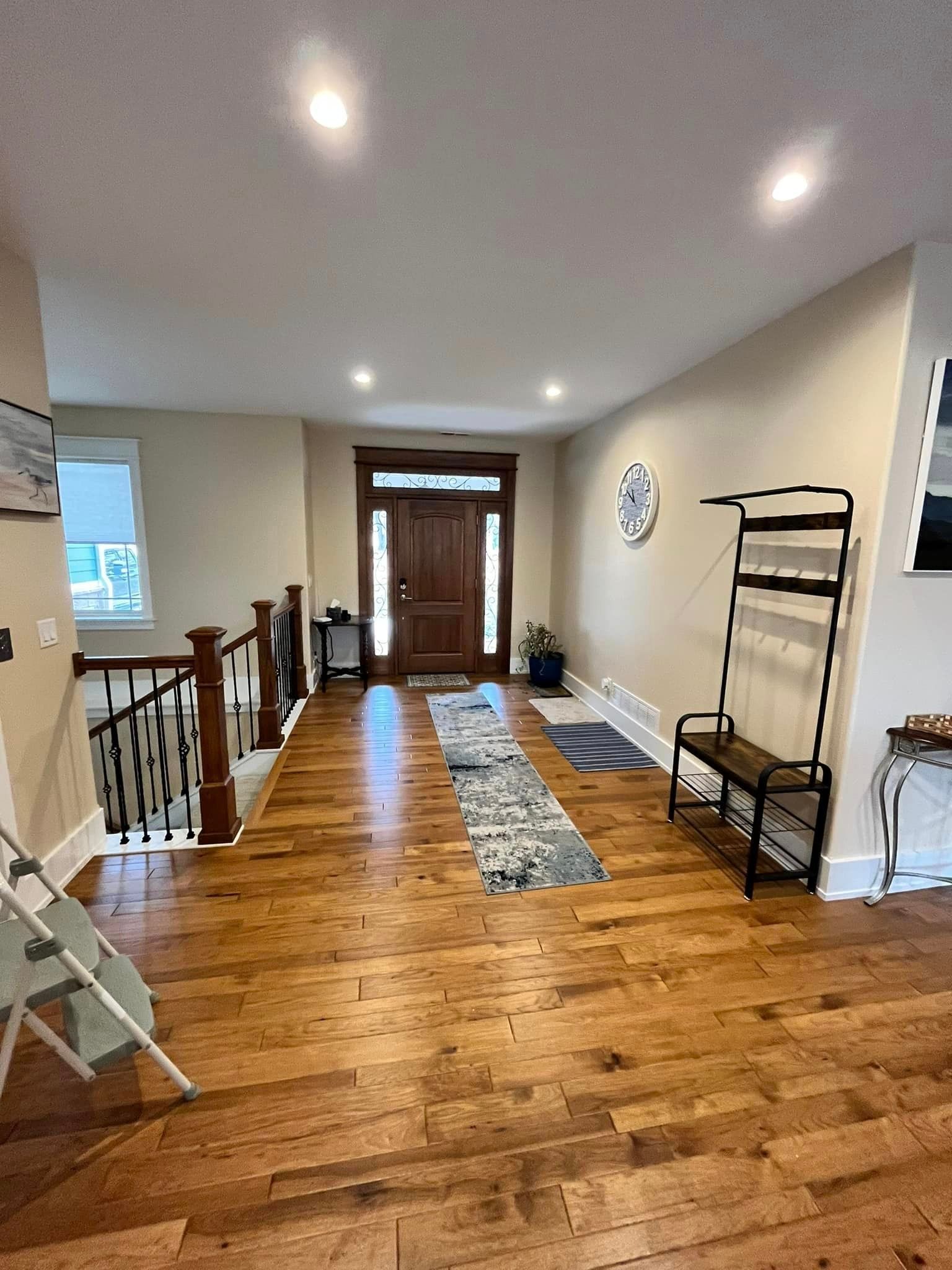 Long hallway with hardwood floors, white walls, runner rug, staircase railing, and a front door at the end.