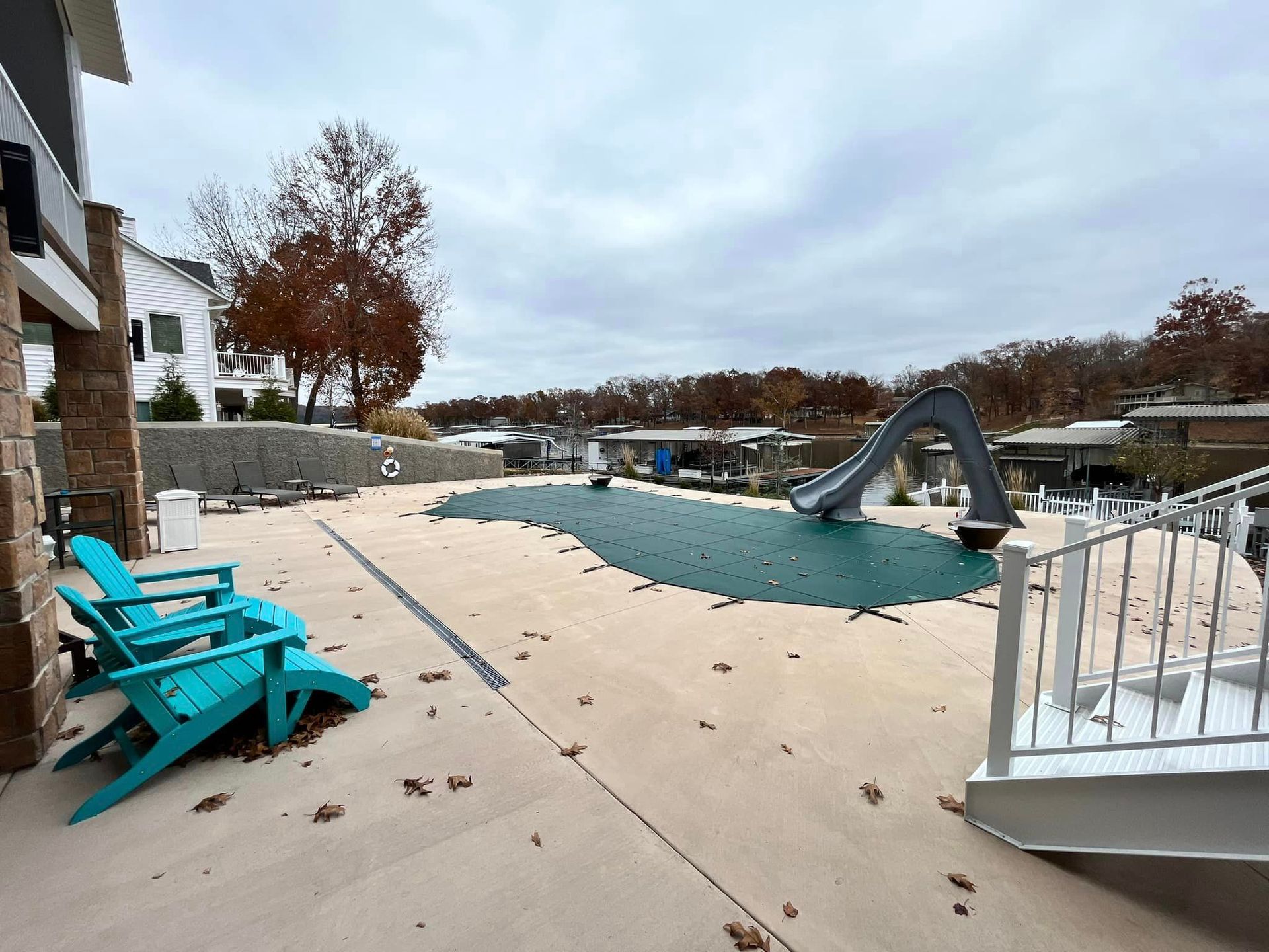 Outdoor pool deck with turquoise chairs, a curving slide, and lounge seating under an overcast sky