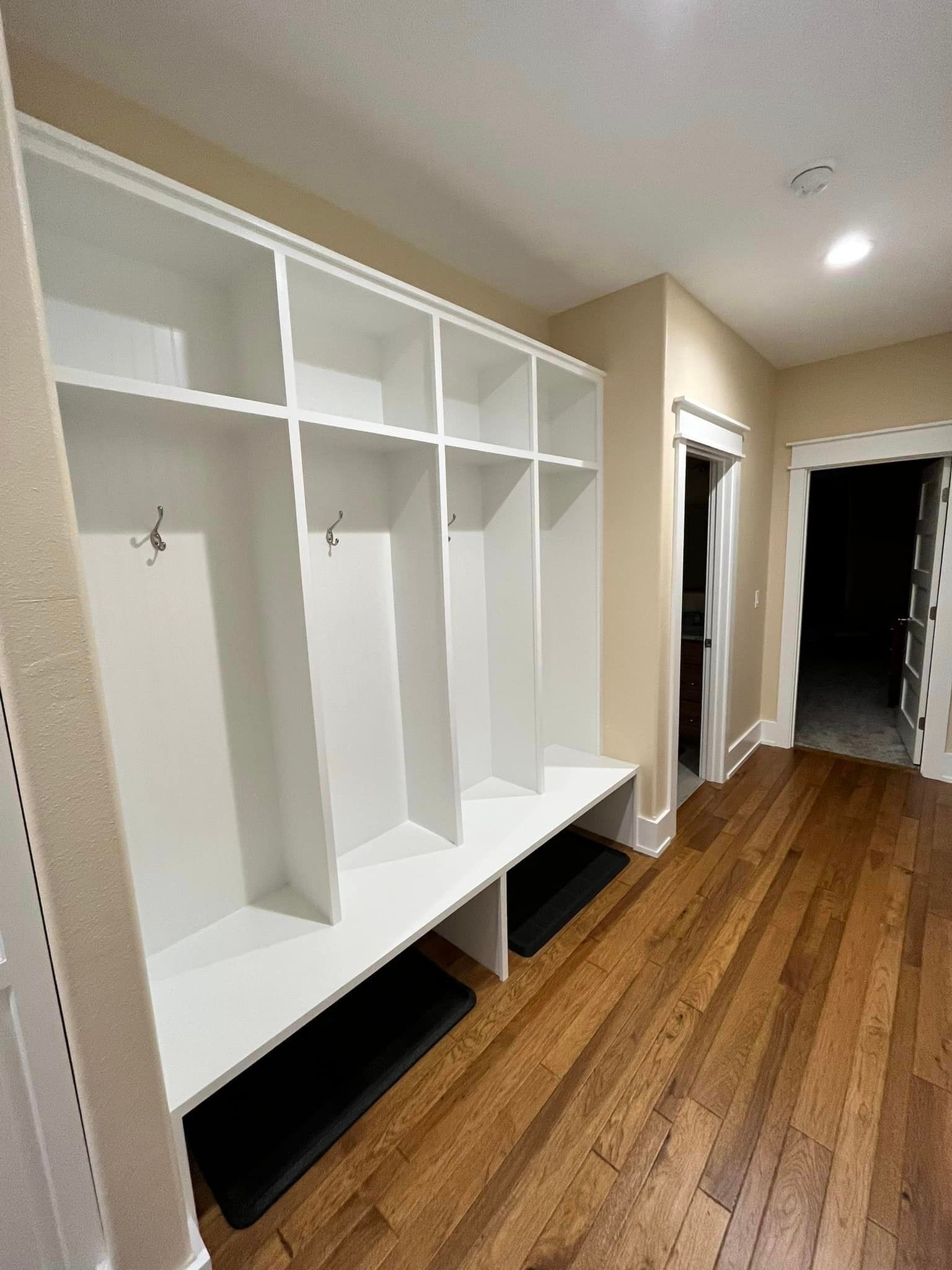White built-in mudroom lockers with bench seating in a hallway with wood floors.