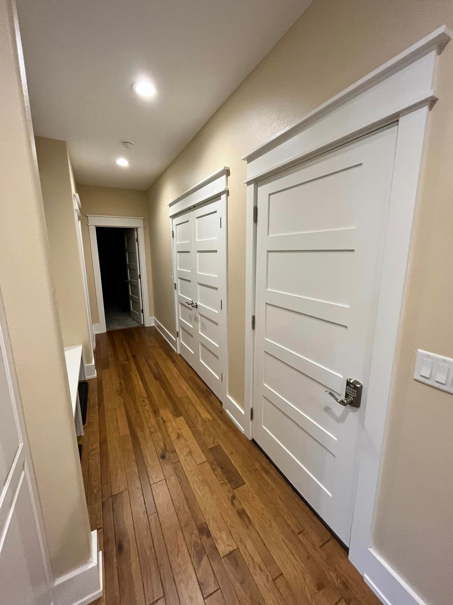 Narrow beige hallway with white doors, wood floor, and recessed ceiling lights