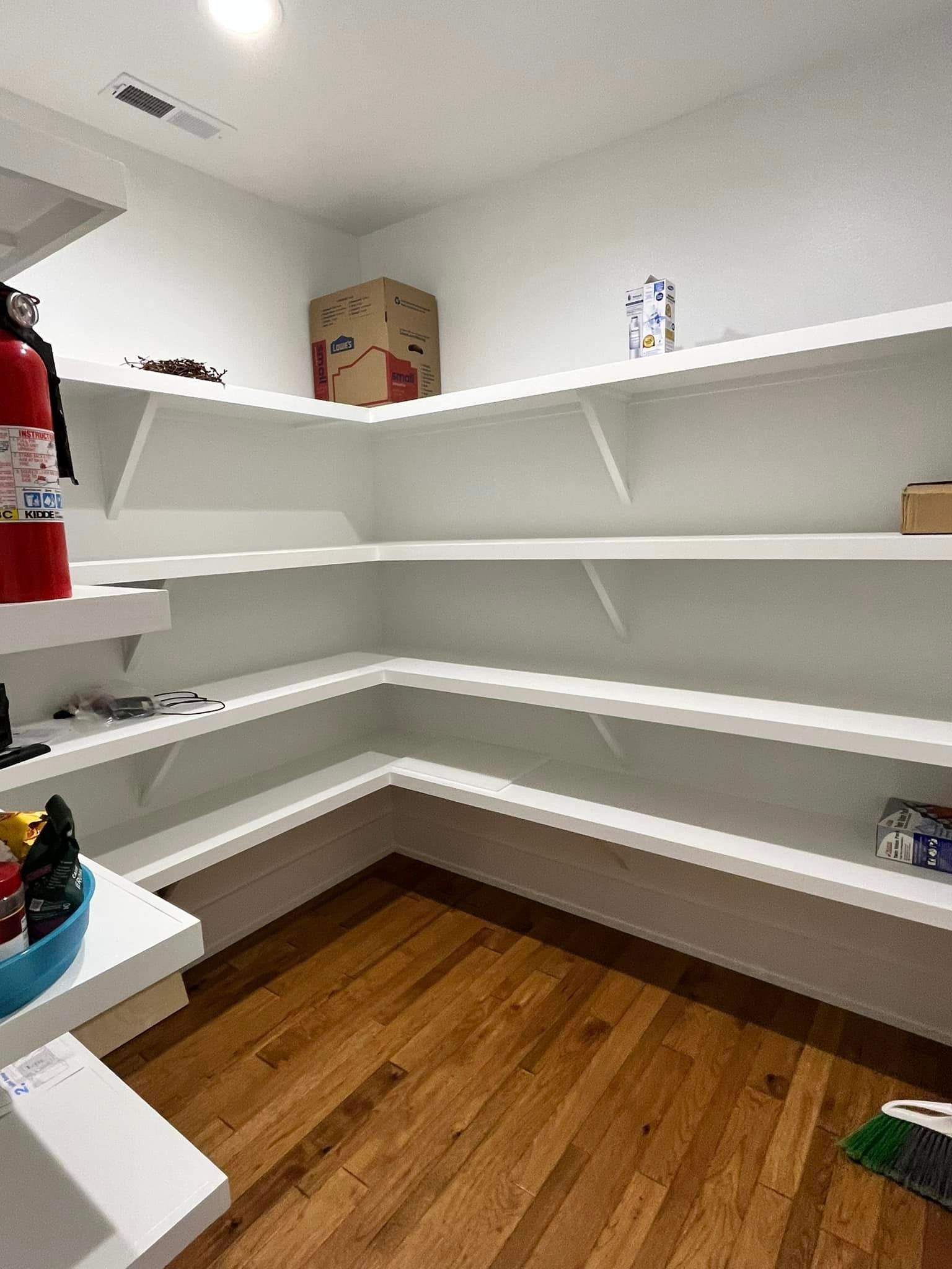 Empty pantry with white shelves, wood floor, and a red fire extinguisher on the left wall.
