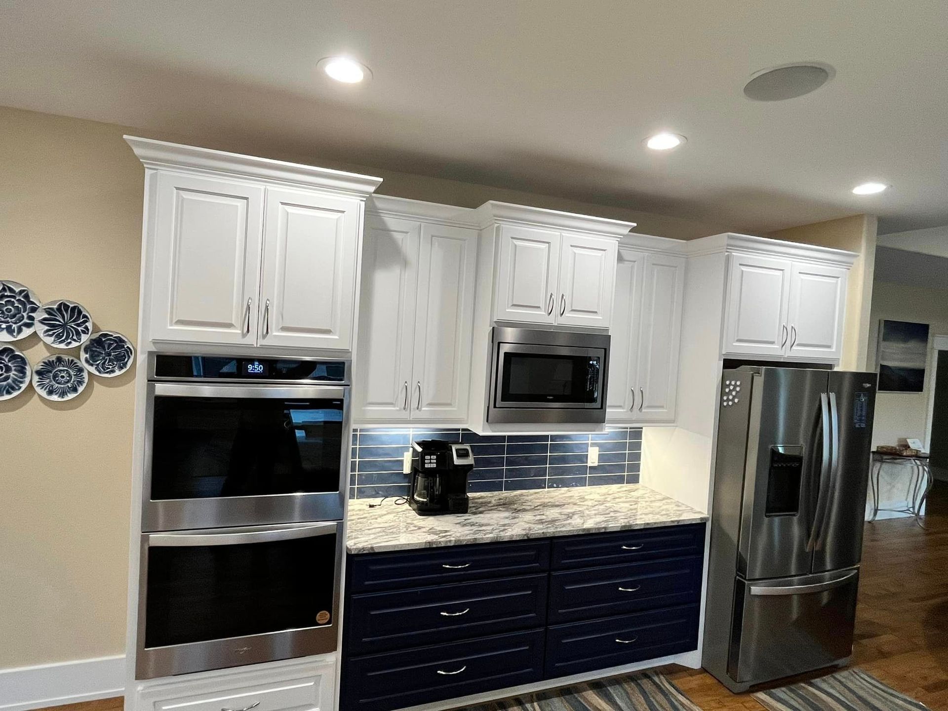Modern kitchen with white and navy cabinets, stainless steel appliances, and recessed ceiling lights