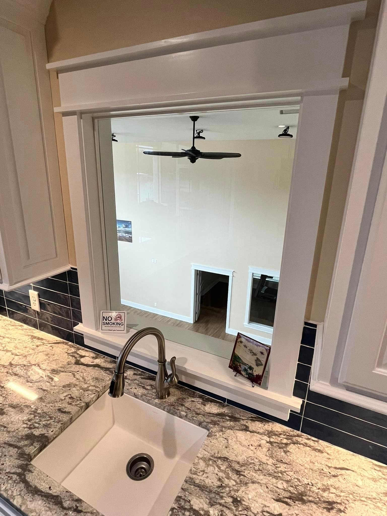 Kitchen sink and granite counter looking through a pass-through to a bright room with a ceiling fan.