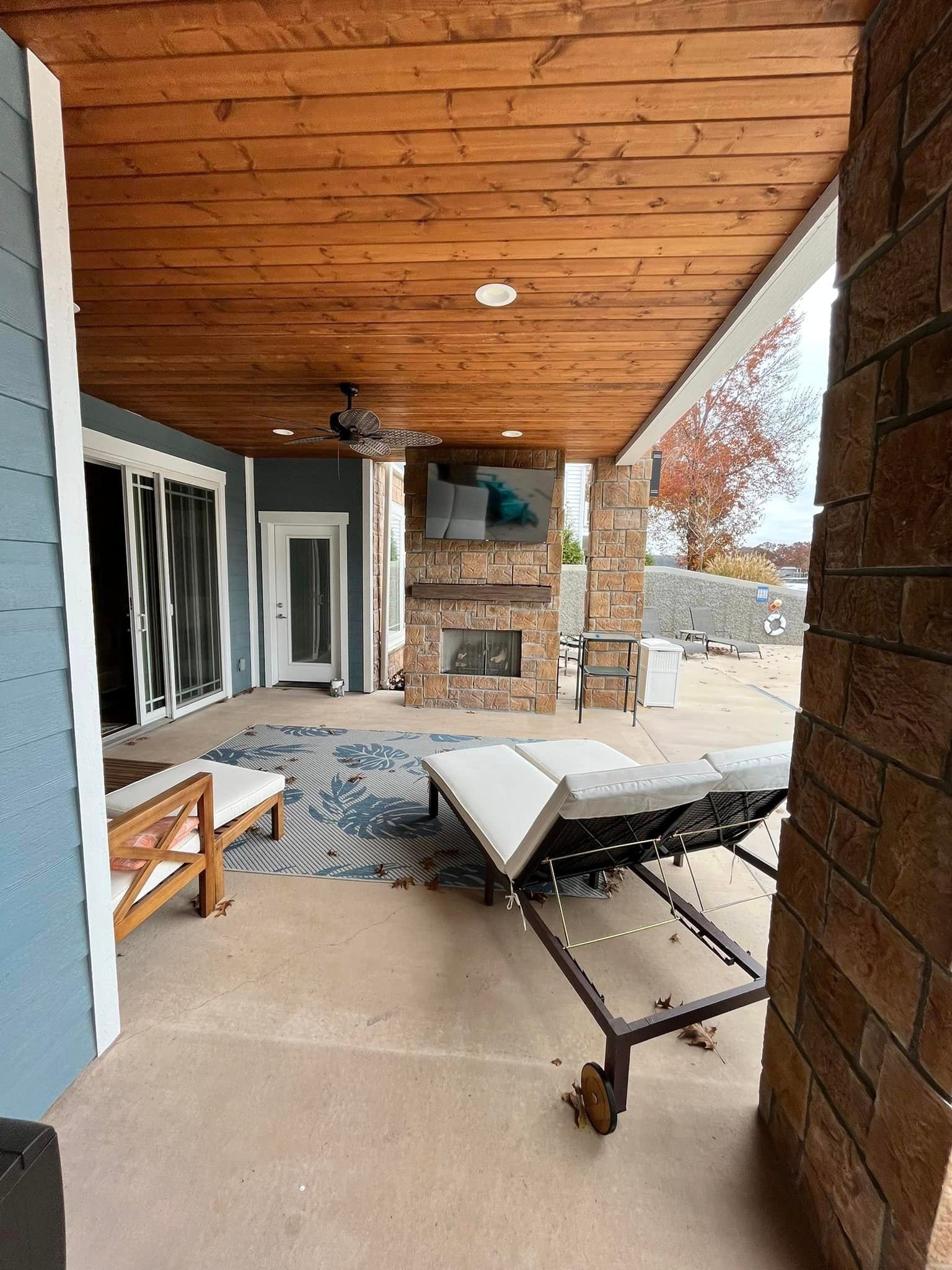 Covered patio with a hammock chair, lounge chair, and brick fireplace beside sliding glass doors