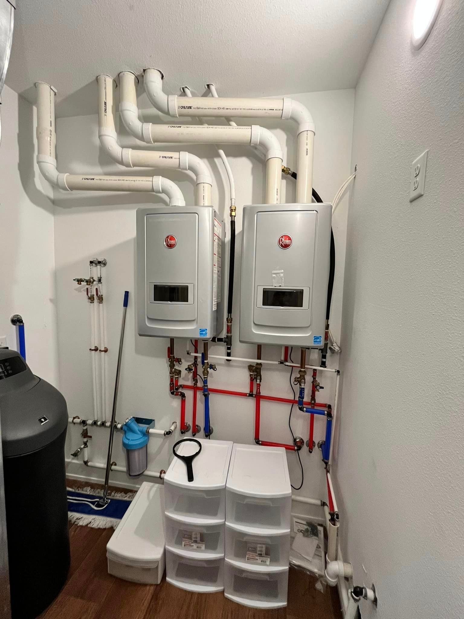 Utility room with two wall-mounted boilers and white plumbing pipes on a narrow wall.