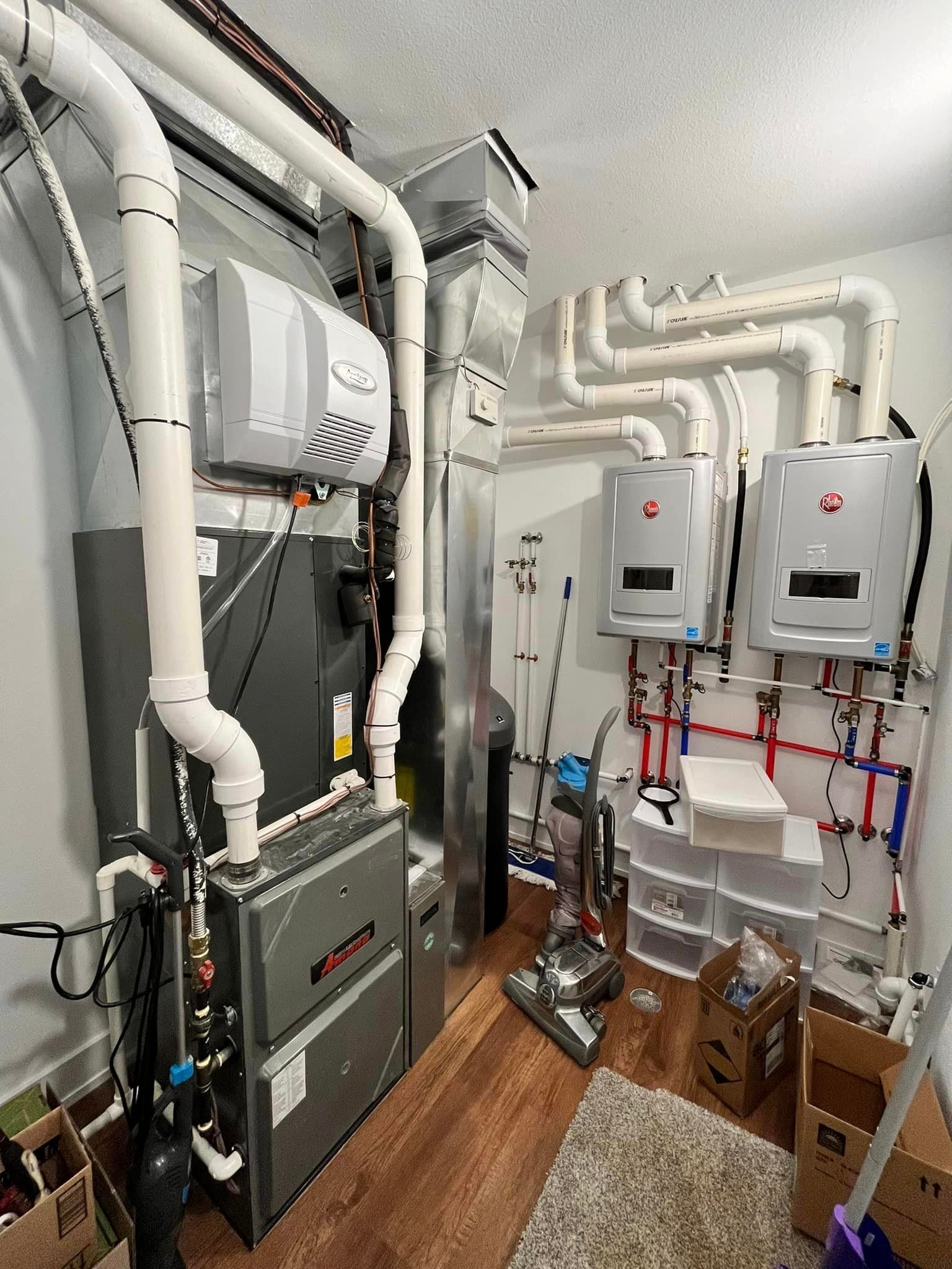 Mechanical room with white pipes, wall-mounted boilers, and a gray furnace on wood flooring.