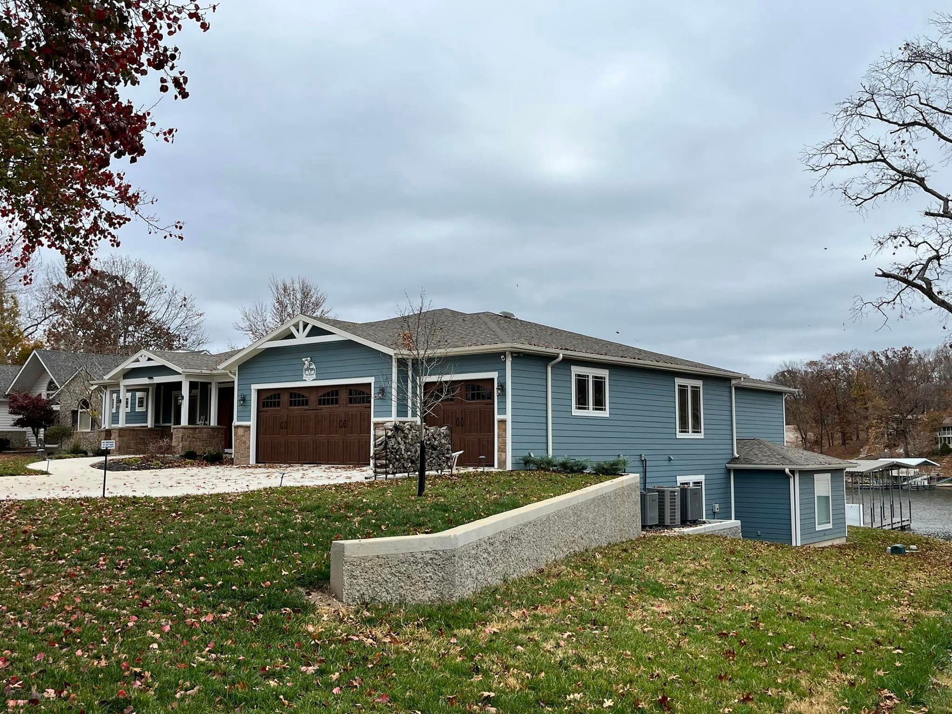 Blue ranch-style house with a two-car garage on a grassy hill under a cloudy sky
