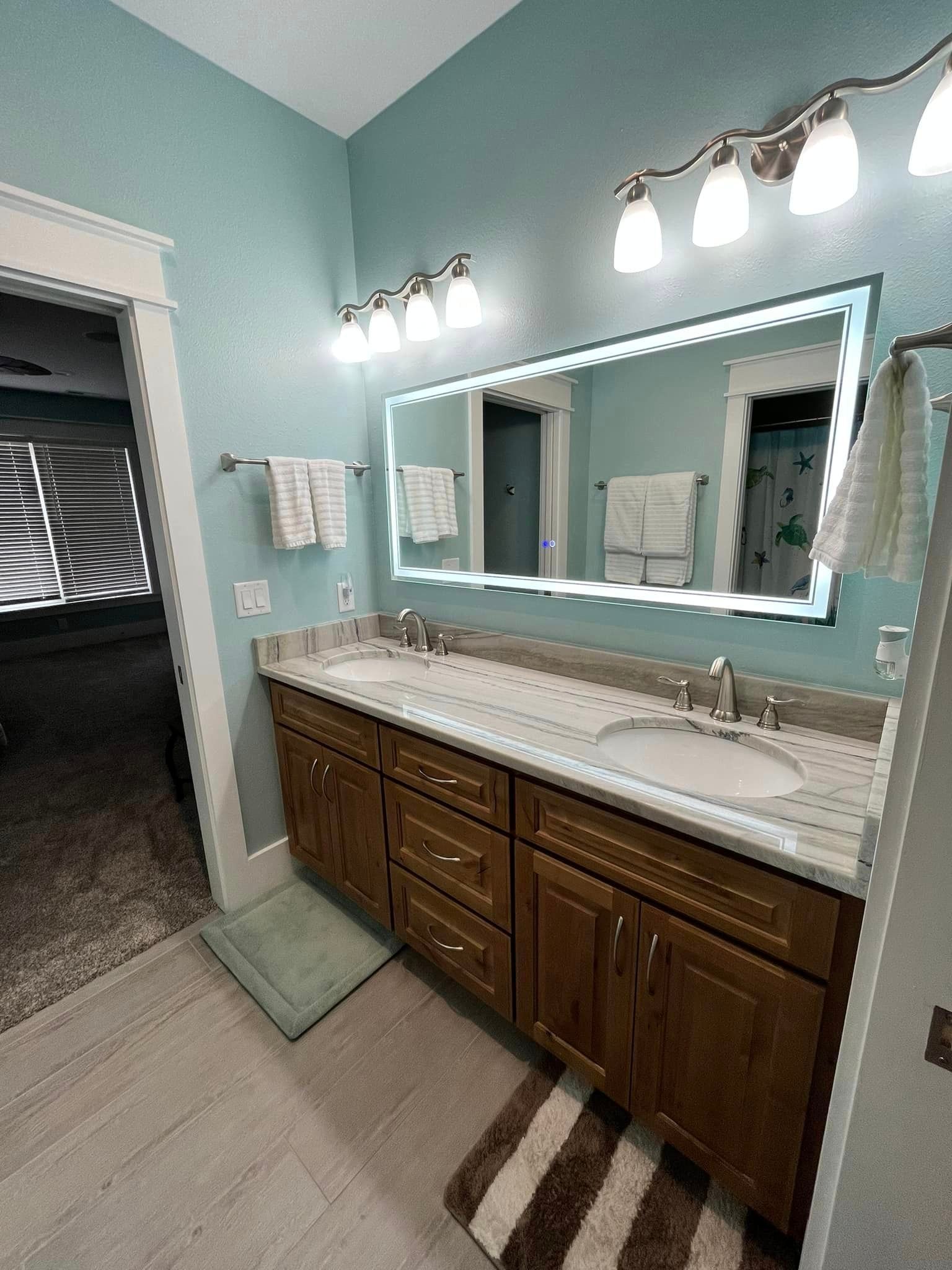 Bathroom vanity with large mirror, double sink, and teal walls, lit by vanity lights