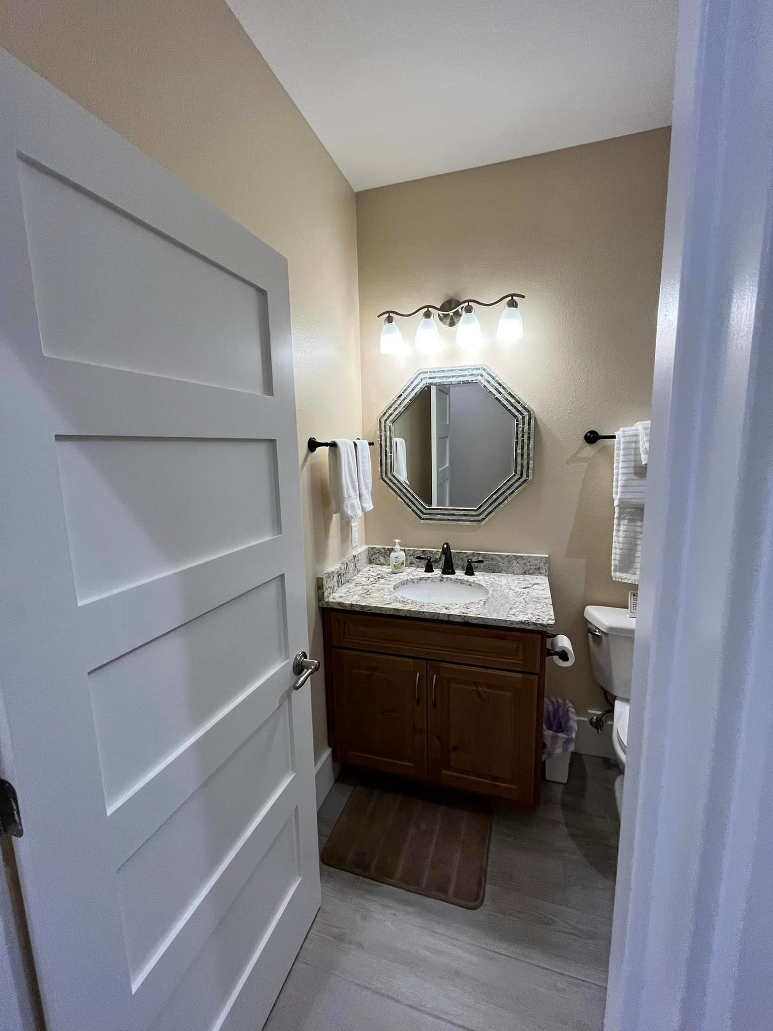 Small bathroom with white door, wooden vanity, octagonal mirror, and light fixture.