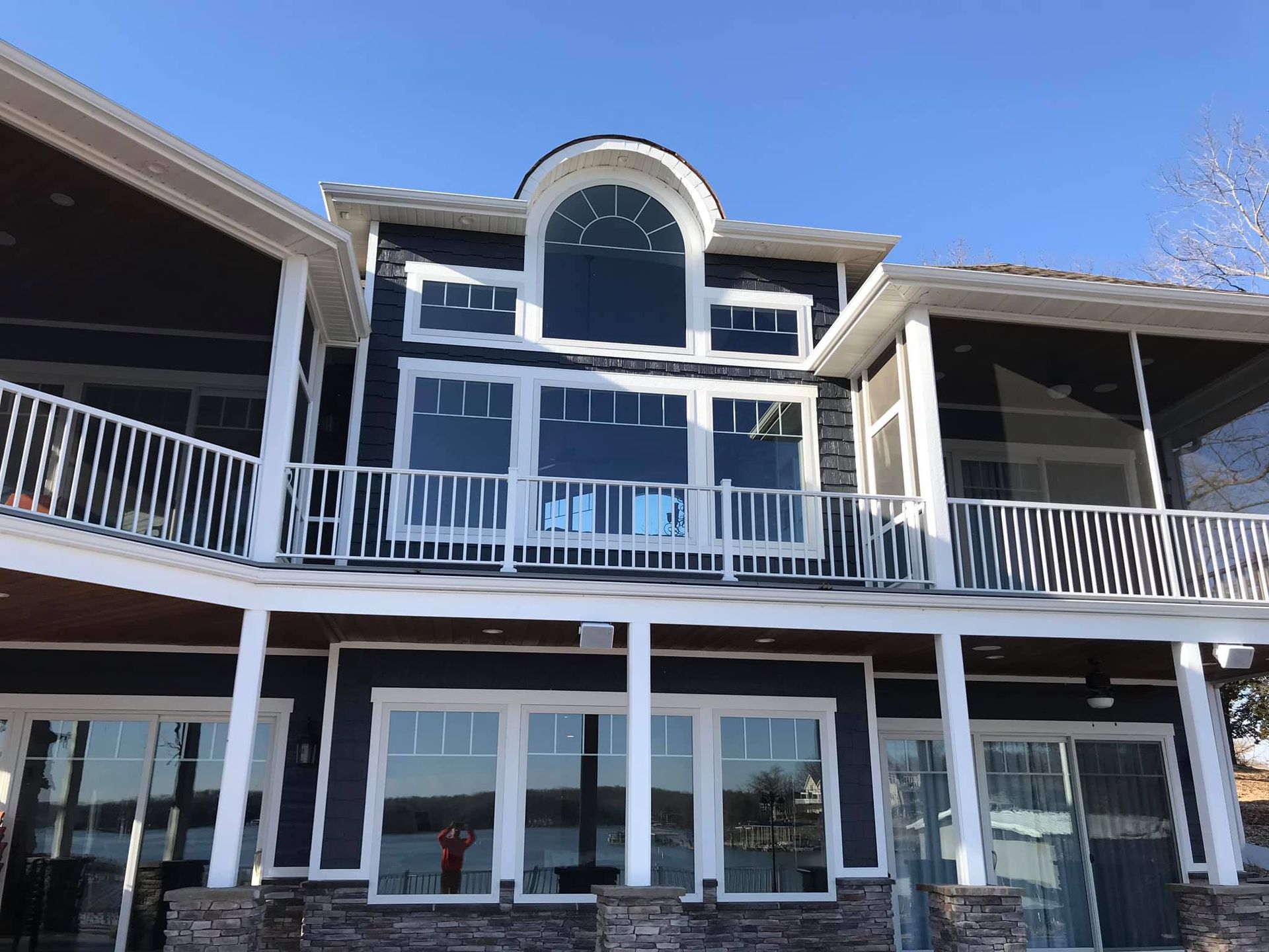 Two-story house with white railings, large windows, and a curved central balcony under a blue sky