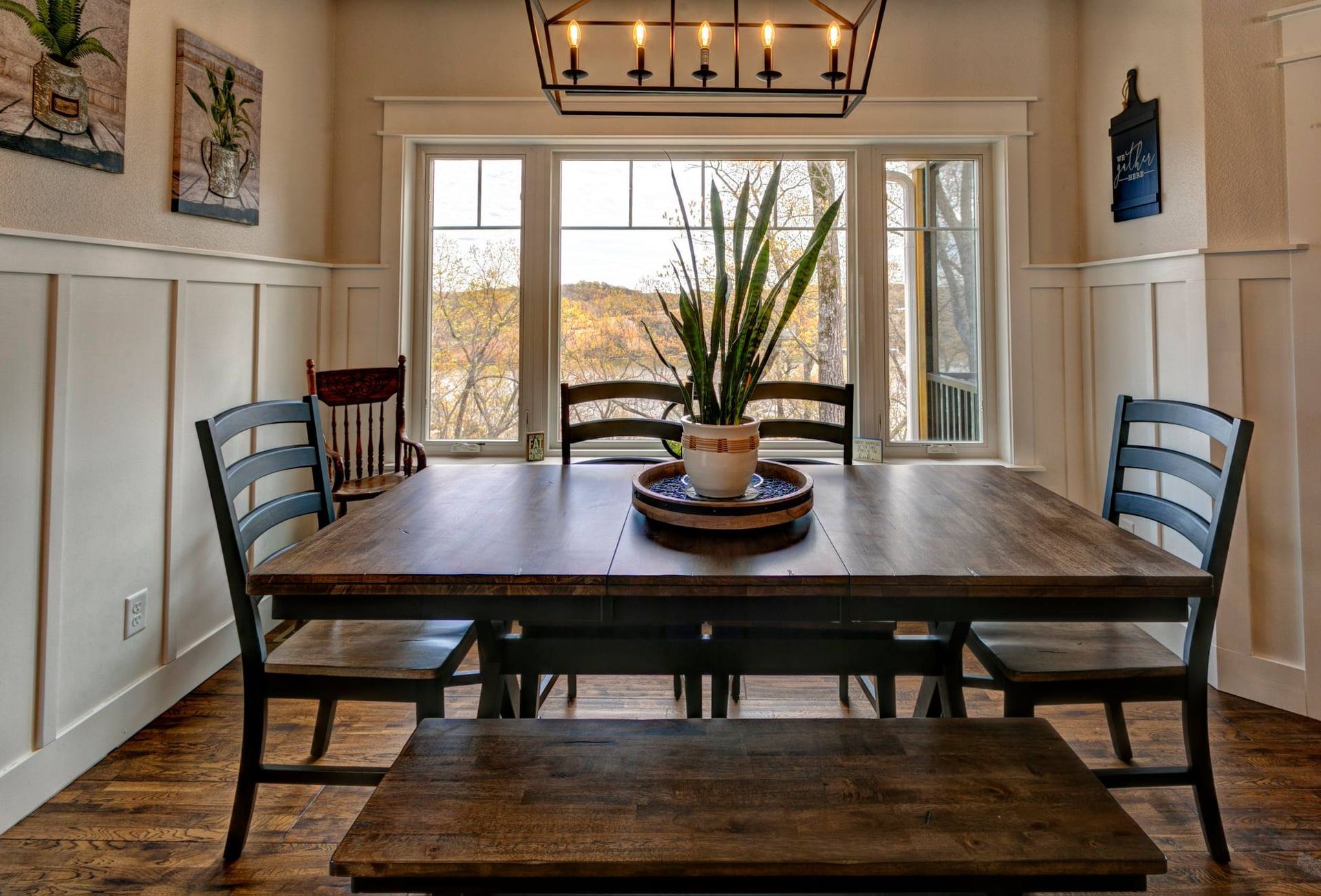 Dining room with dark wood table, benches, and large window overlooking a bright landscape.