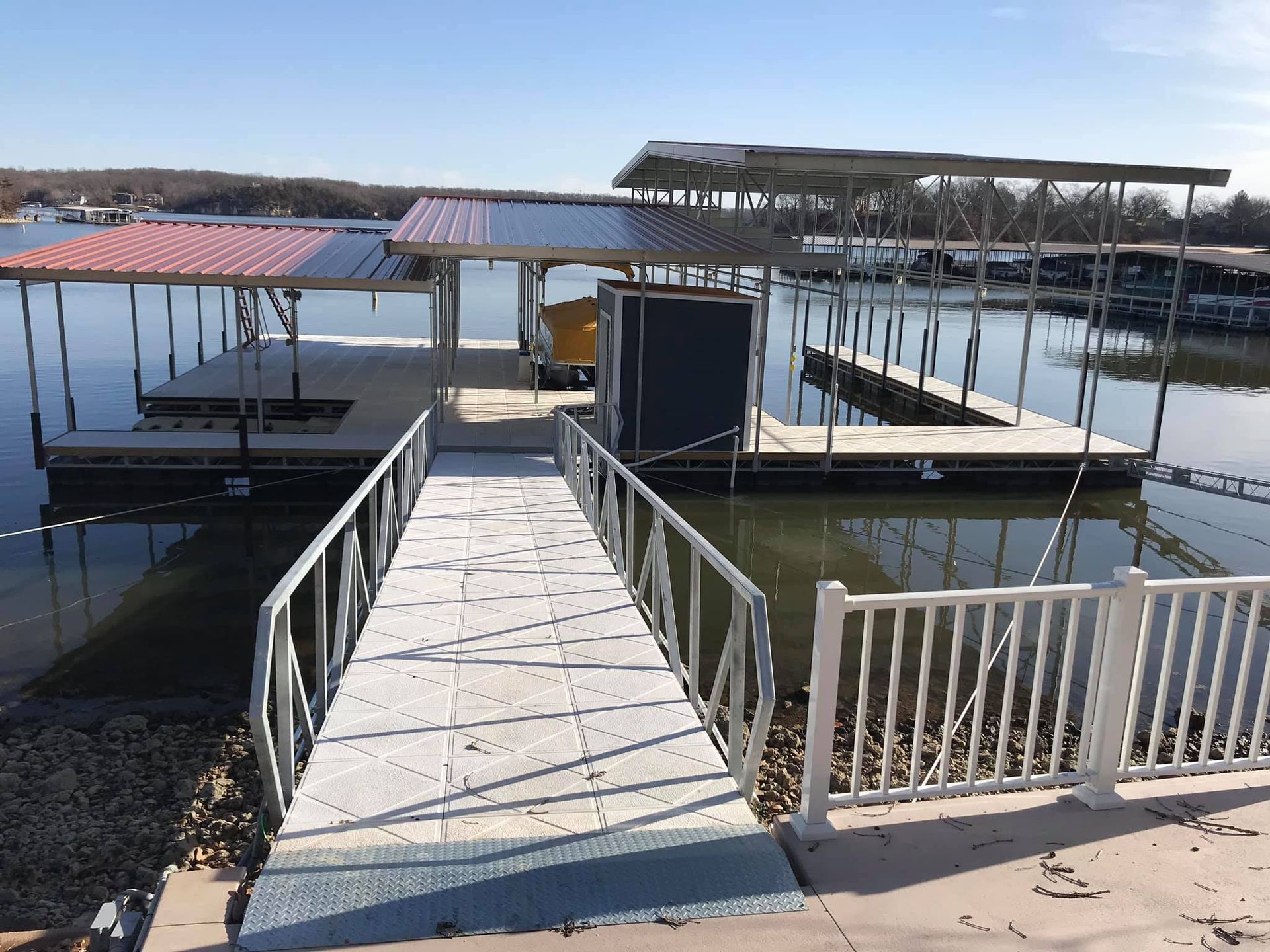 Wooden dock walkway leading to covered boat slips on calm water under a clear sky.