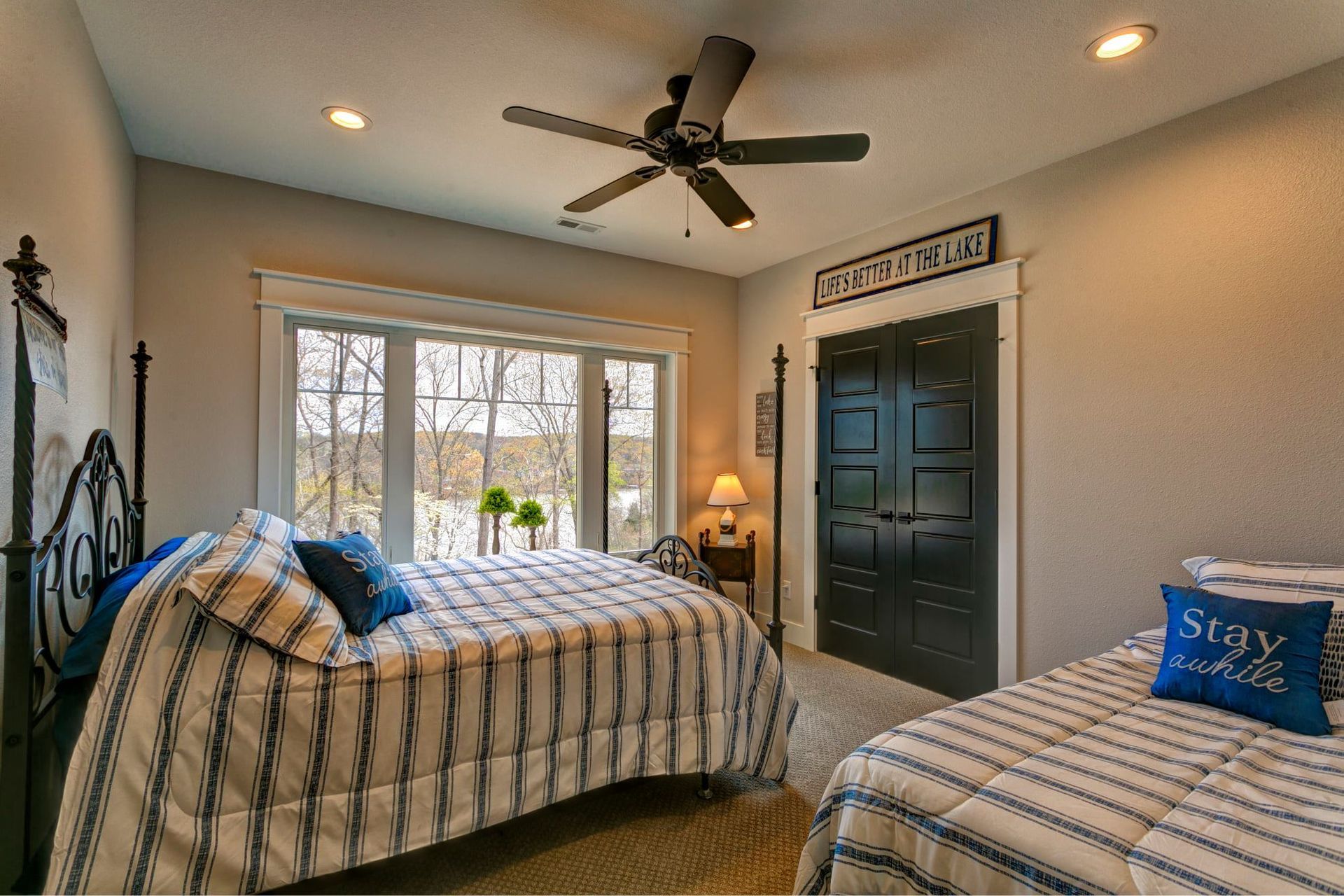 Bright bedroom with two beds, window, ceiling fan, and dark blue door