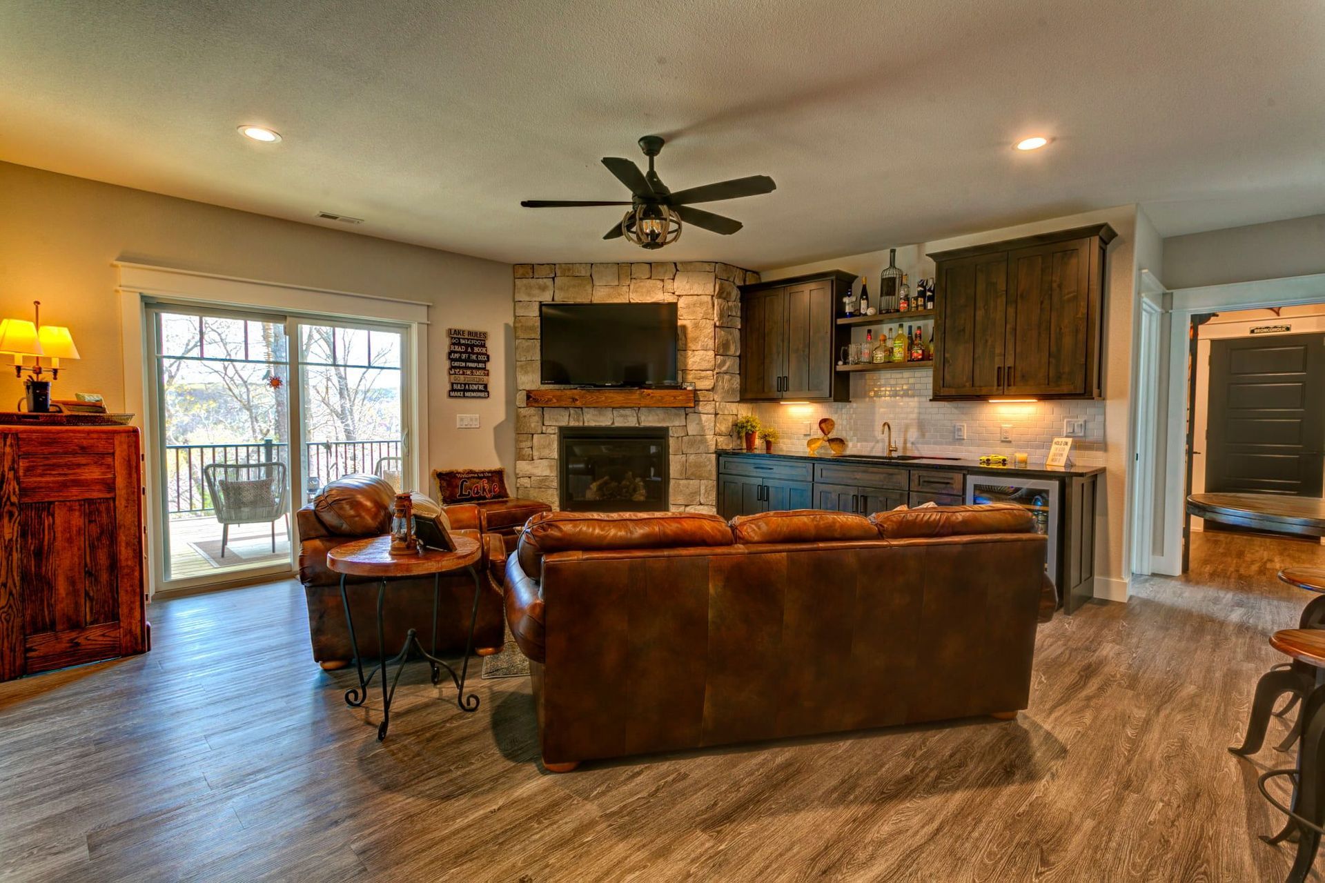 Cozy open-concept living room with leather sofa, fireplace, ceiling fan, and kitchen bar stools