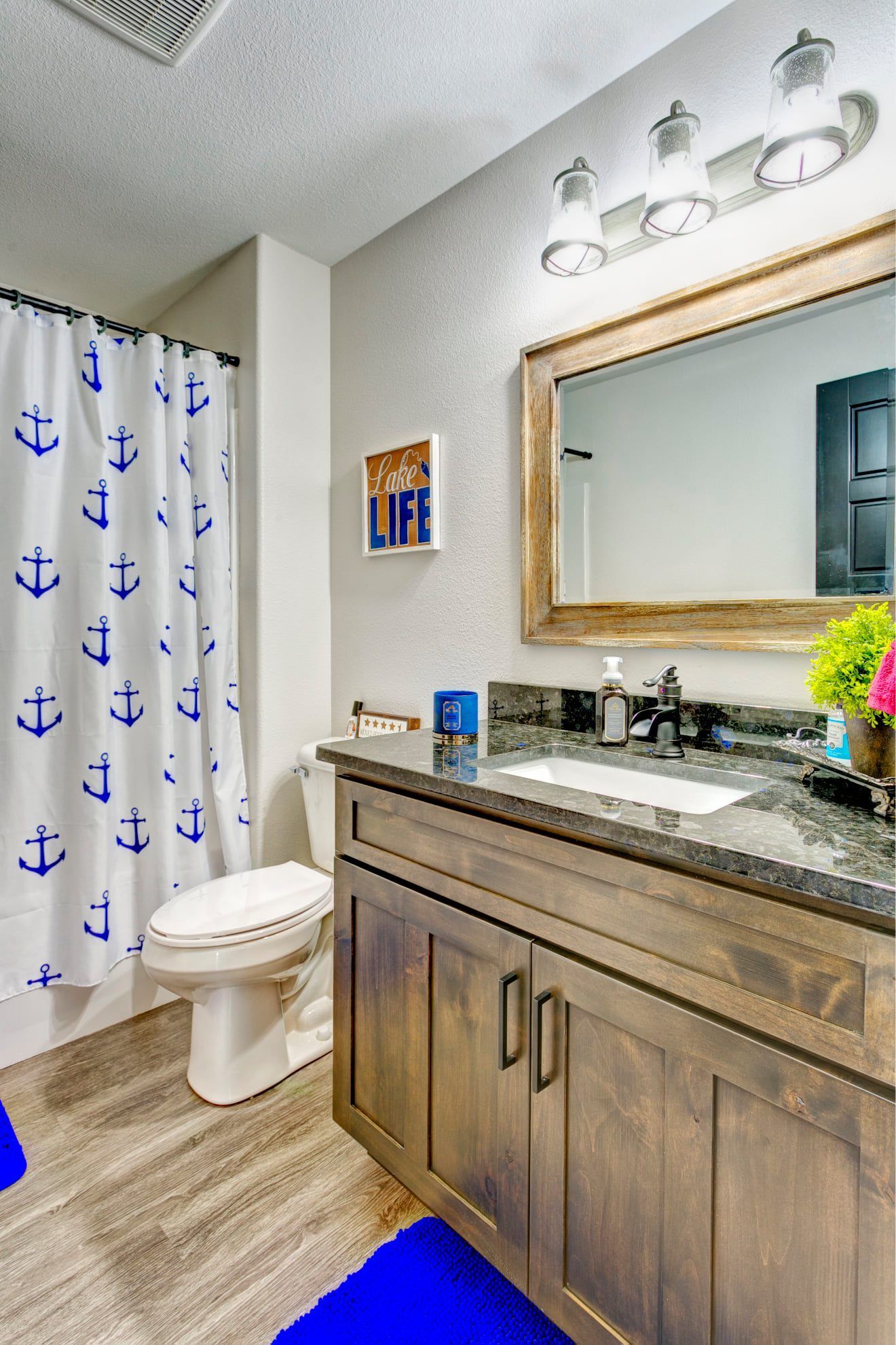 Modern bathroom with wood vanity, mirror, toilet, and shower curtain with blue anchors