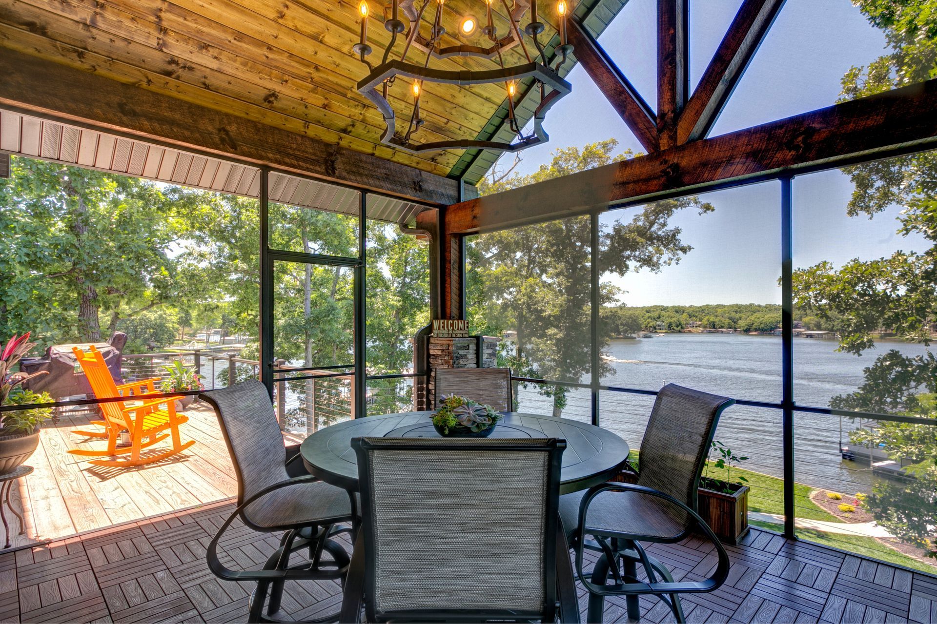 Screened porch with table and chairs overlooking a lake, lit by string lights at sunset