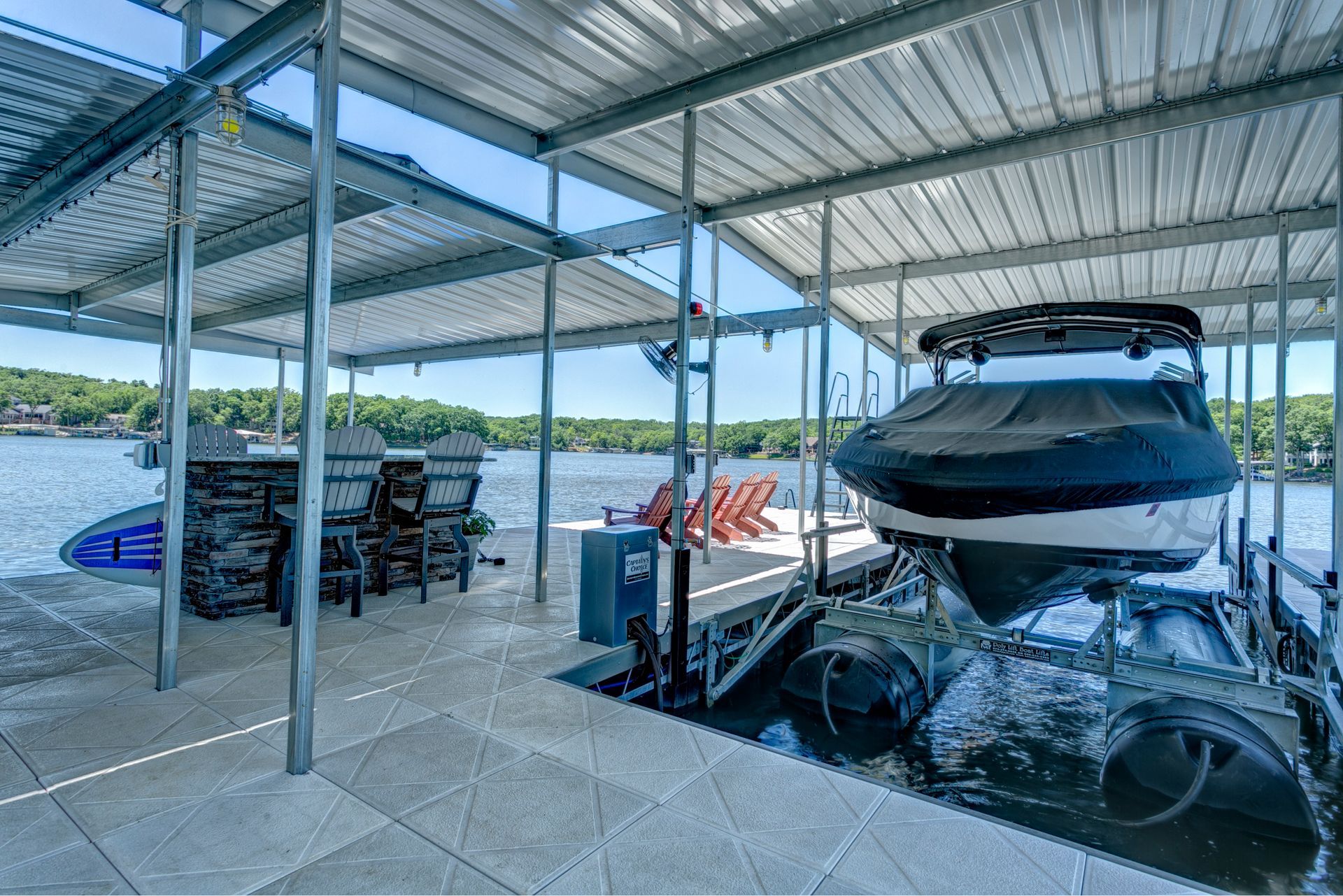 Covered boat dock with a black speedboat on a trailer and stacked chairs by the water.