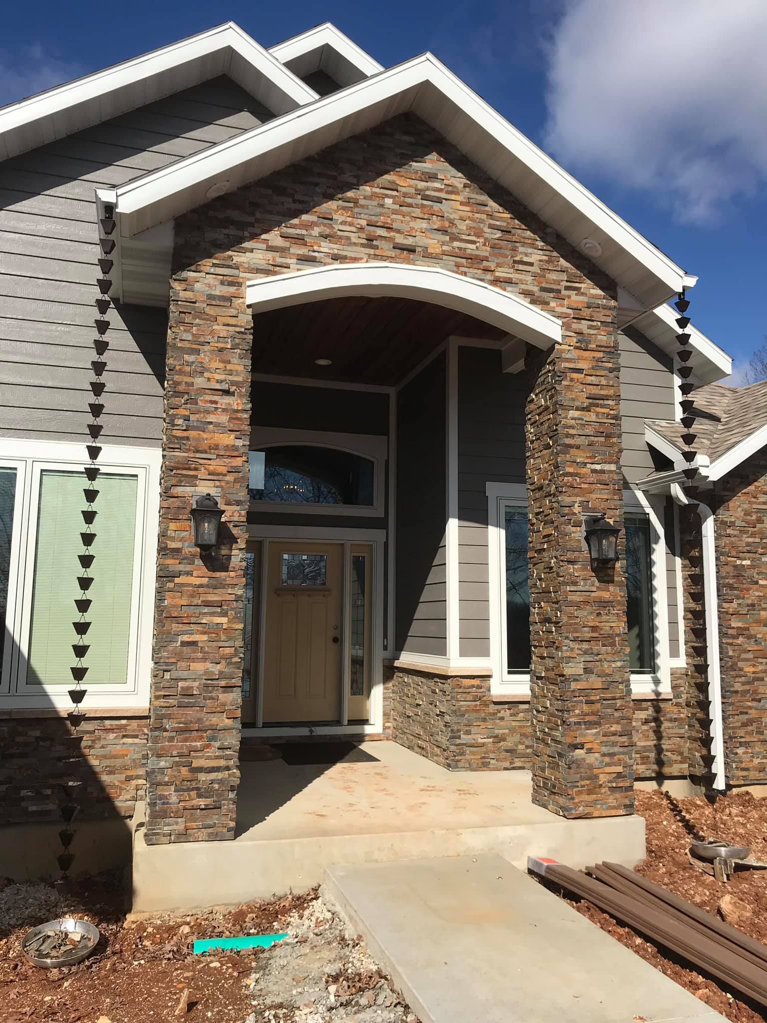Front entrance of a house under construction with stone columns, arched porch, and unfinished landscaping