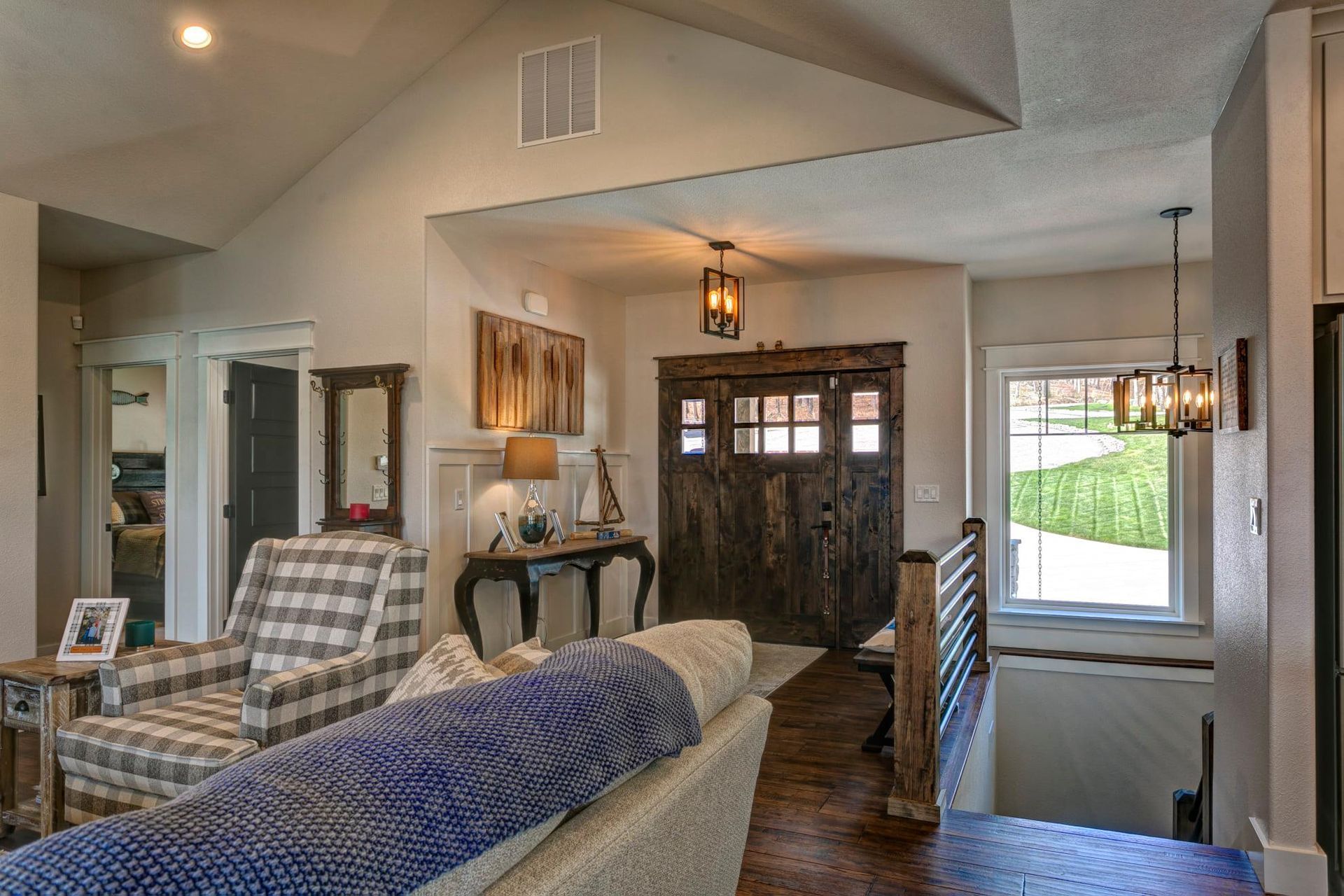Living room with plaid armchair, sofa, front door, and staircase in a bright home interior