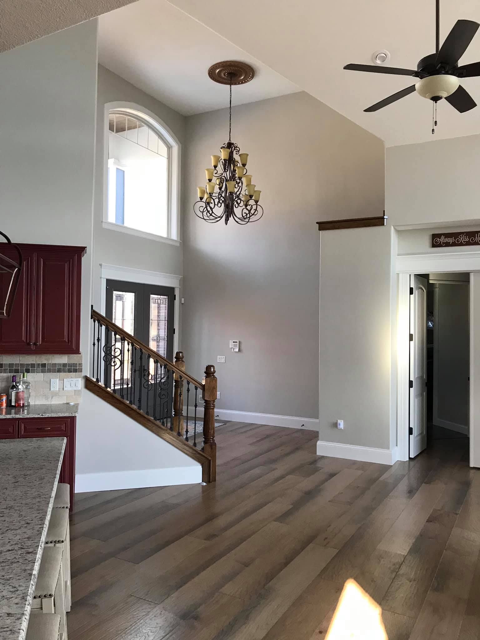 Bright living room with vaulted ceiling, chandelier, stairs, kitchen corner, and wood floor
