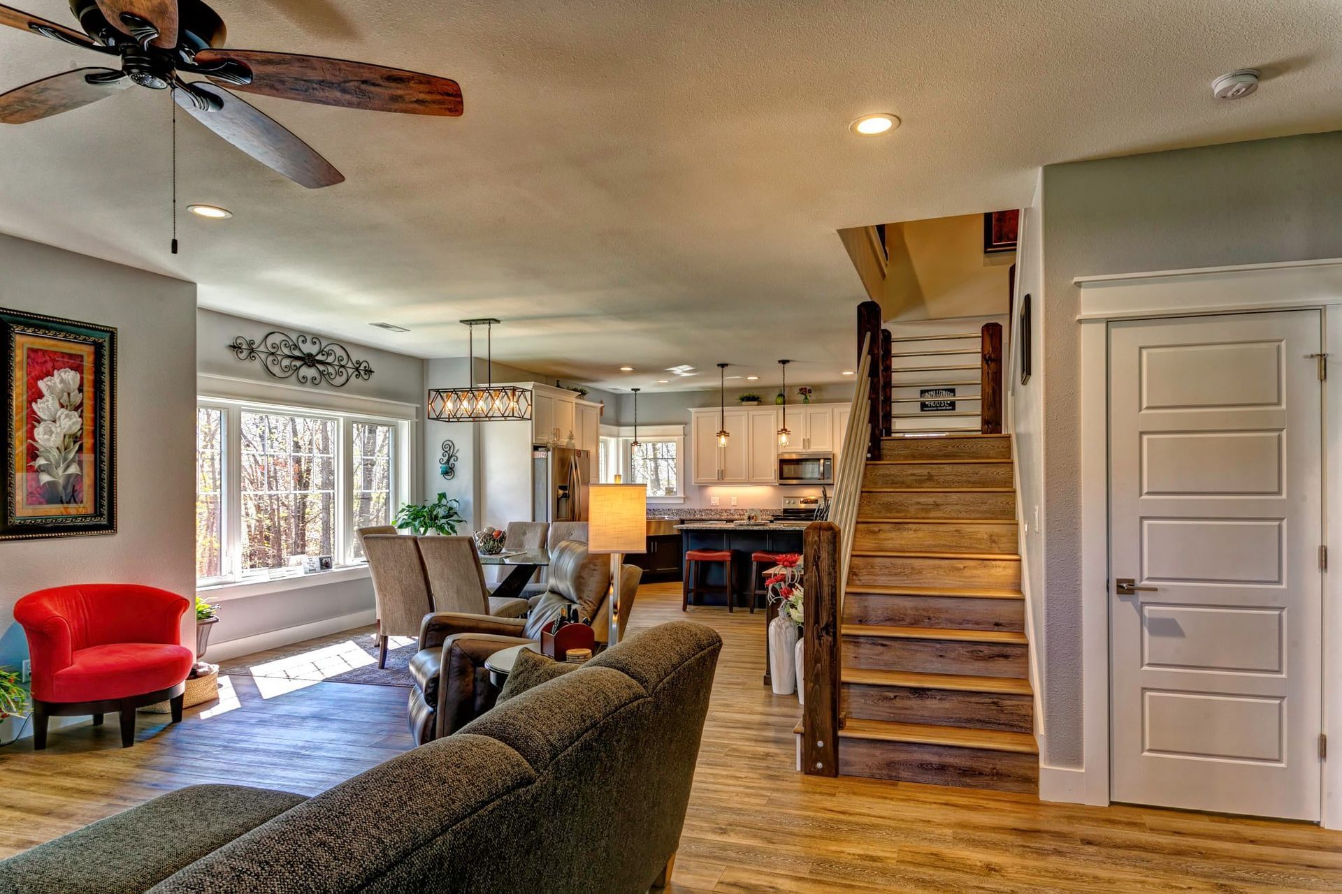 Open-concept living room with wood floors, staircase, ceiling fan, and red accent chair