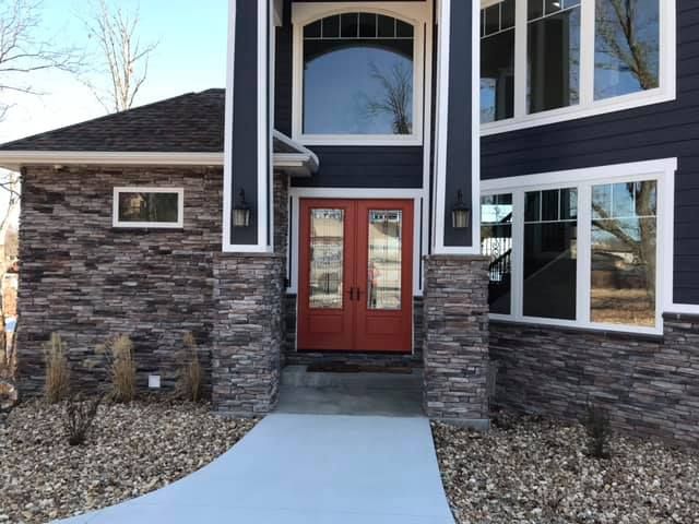 Front entrance of a modern house with stone siding, red double doors, and a curved concrete walkway.