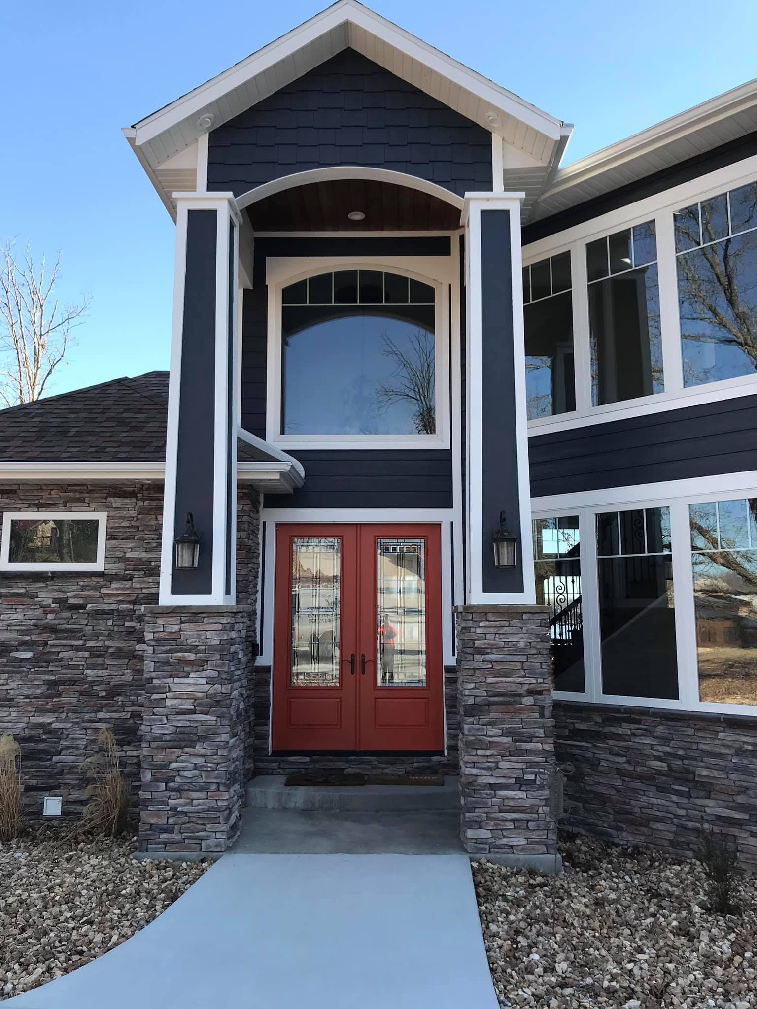 Front entrance of a modern house with red double doors, stone facade, and tall black-and-white columns.