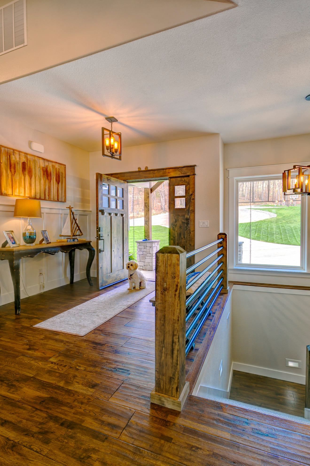 Bright entry hall with wooden floors, staircase railing, front door, and a dog by the entrance