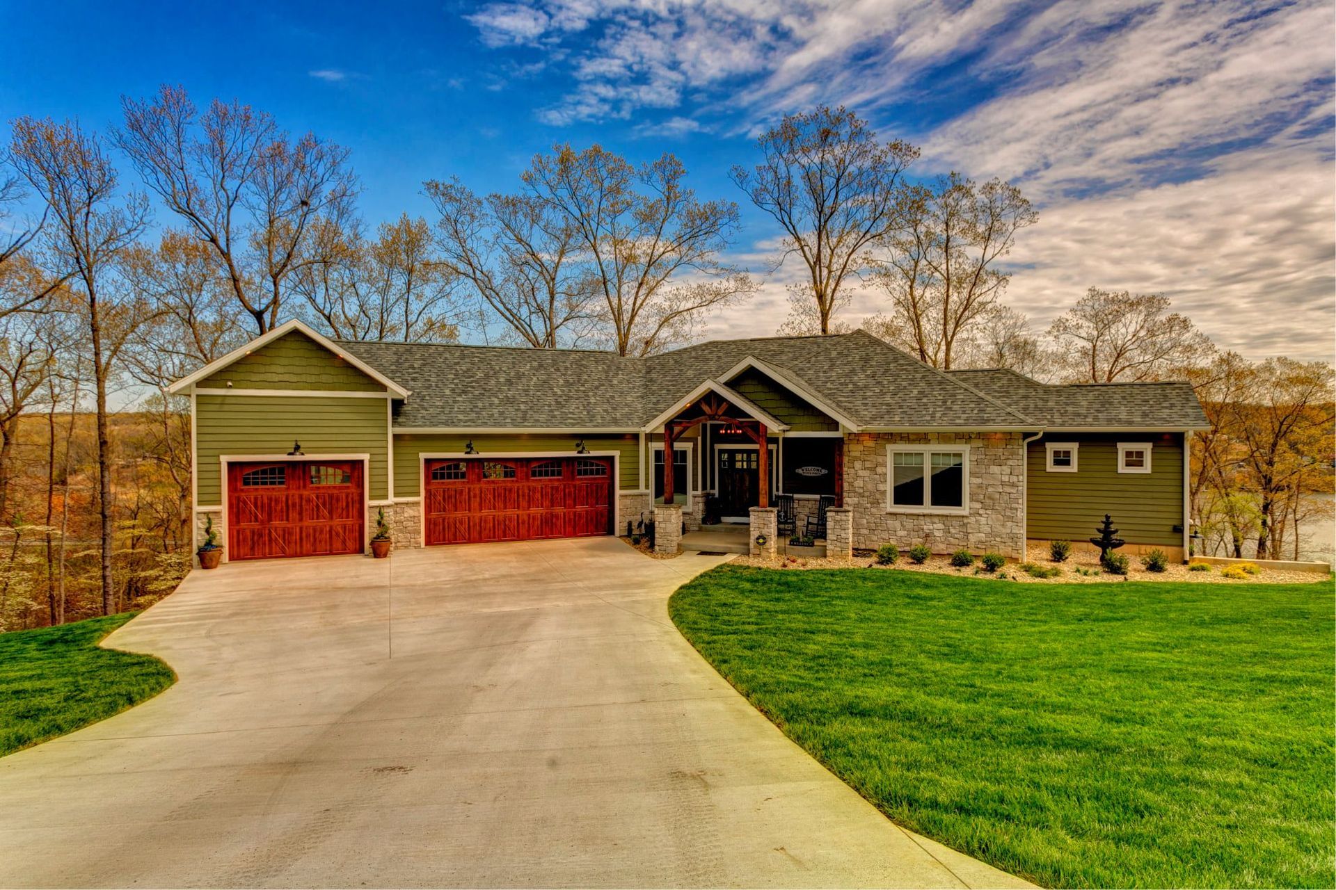 Stone house with red garage doors and a curved driveway, set on a grassy hillside under a blue sky.