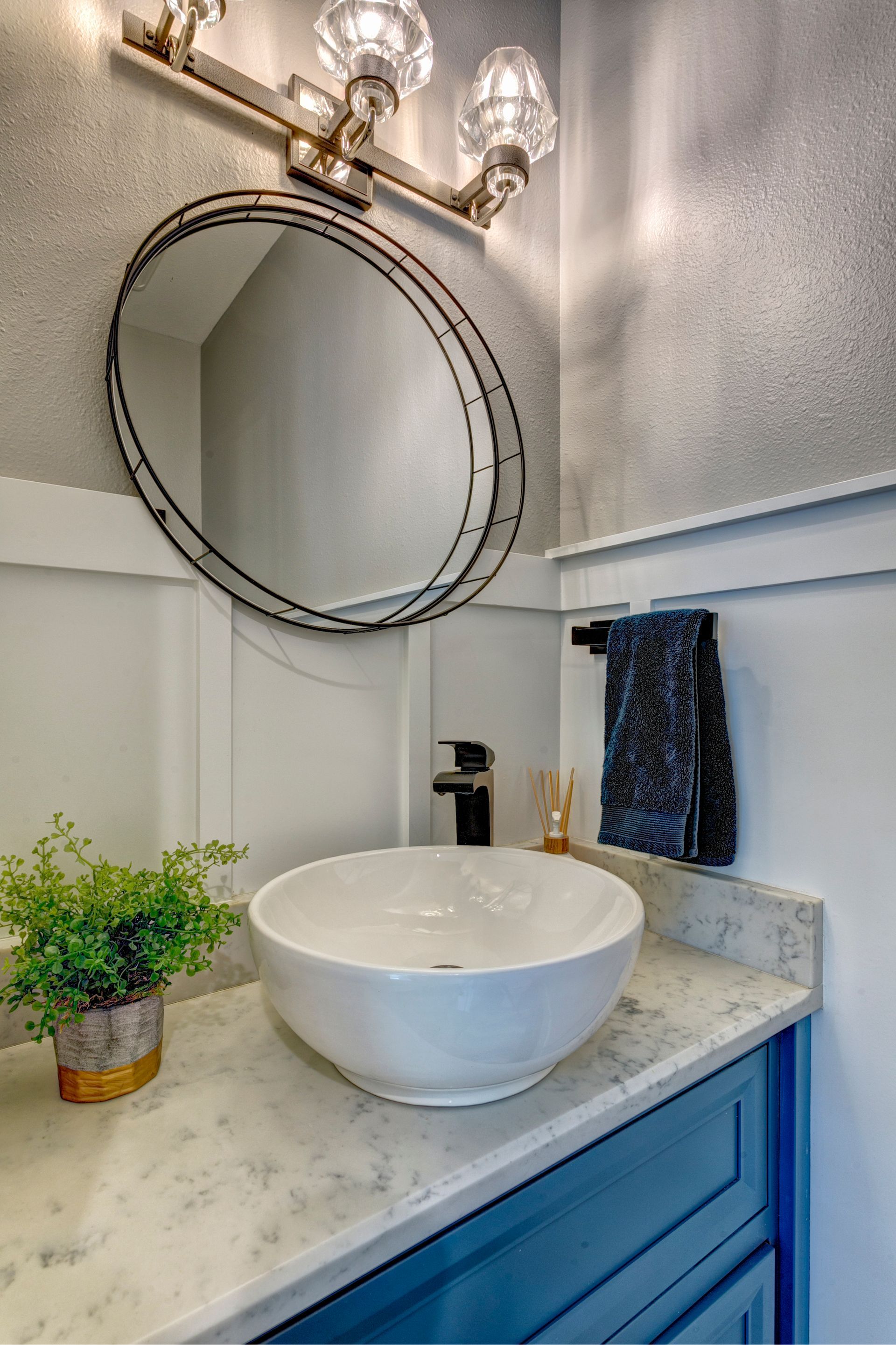 Bathroom vanity with round mirror, white sink, blue cabinet, and wall sconce lights