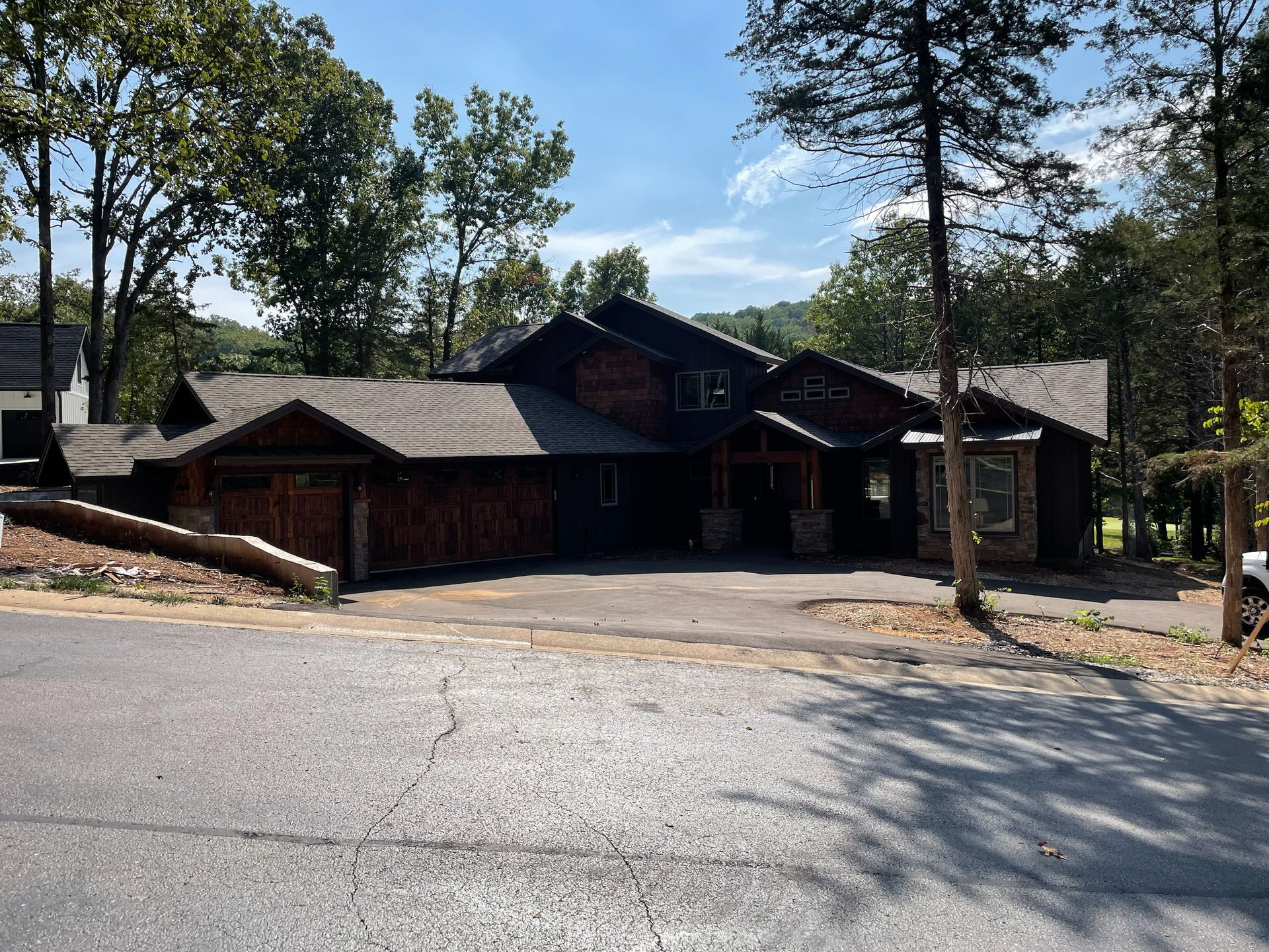 Wooden lodge-style house with a covered entrance, surrounded by trees and a paved driveway