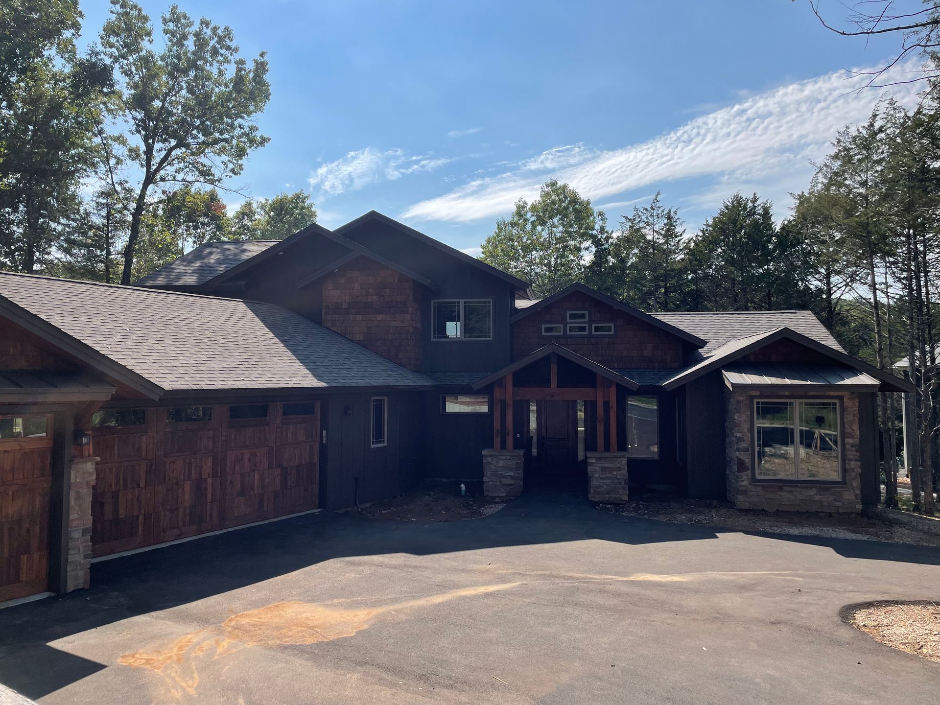 Large rustic cabin with wood siding, stone entry, and paved driveway under a blue sky