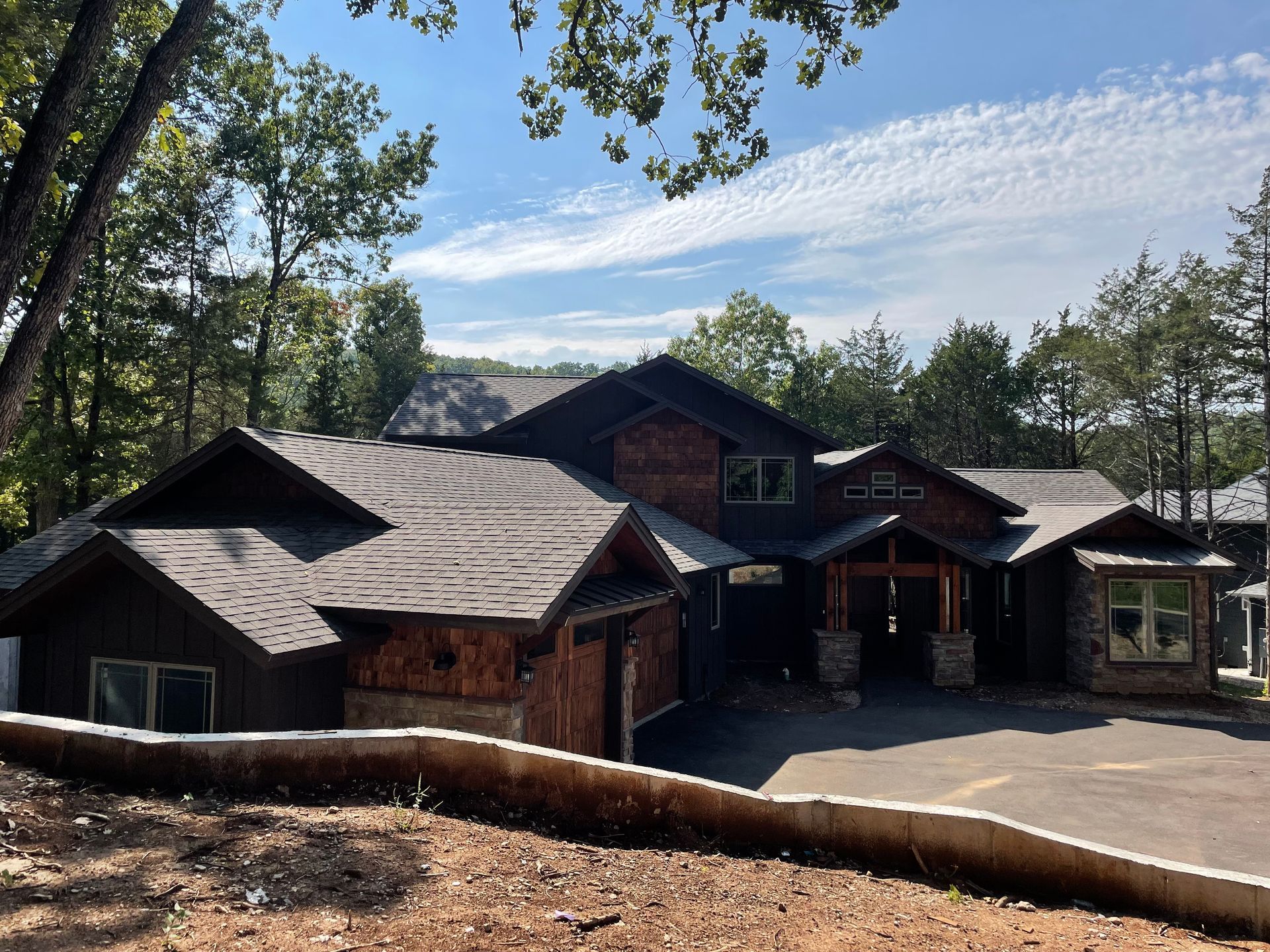 Large rustic lodge with a dark roof and stone facade, surrounded by trees under a blue sky