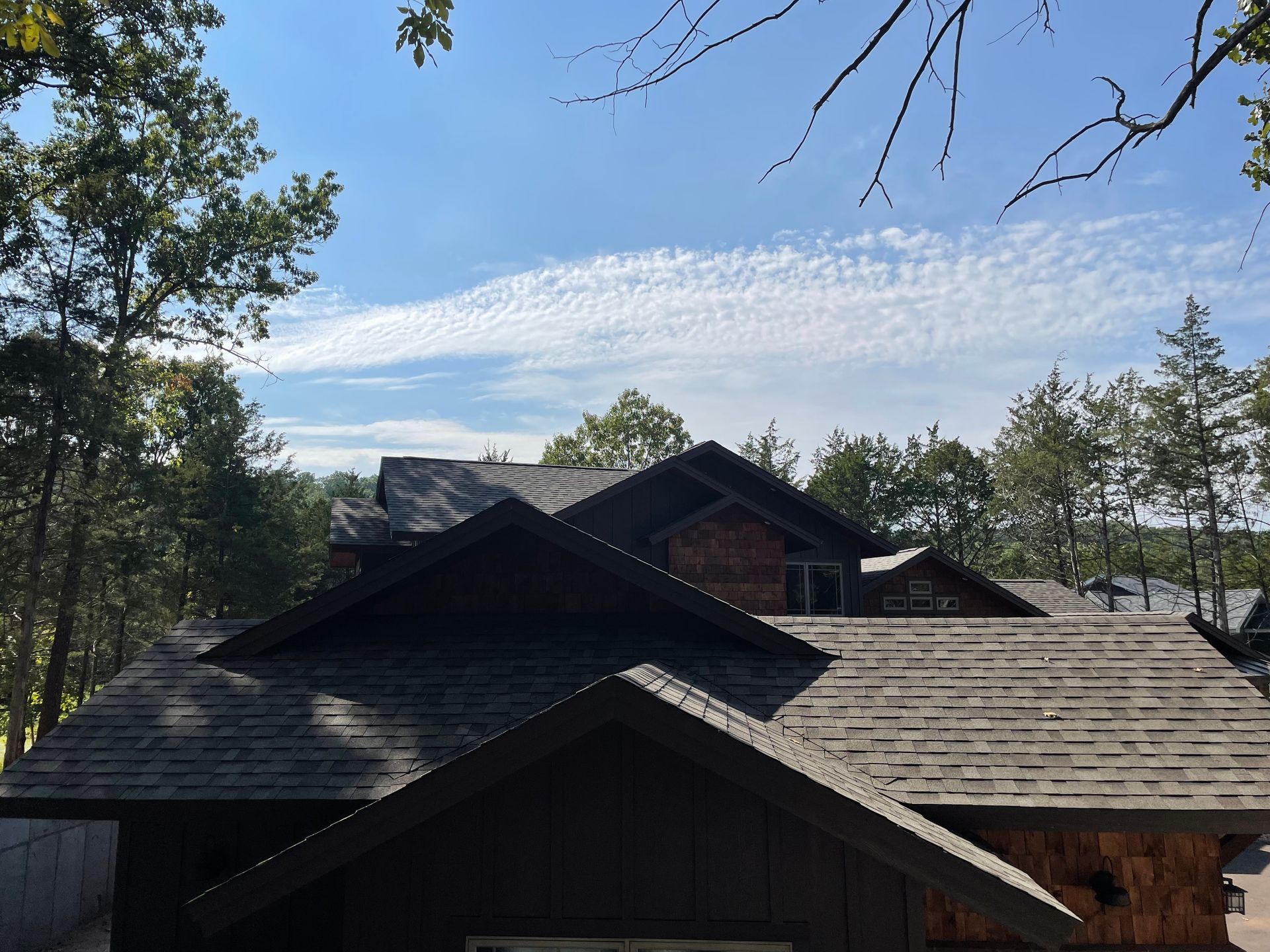 Wooden cabin rooftops among trees under a blue sky with wispy clouds