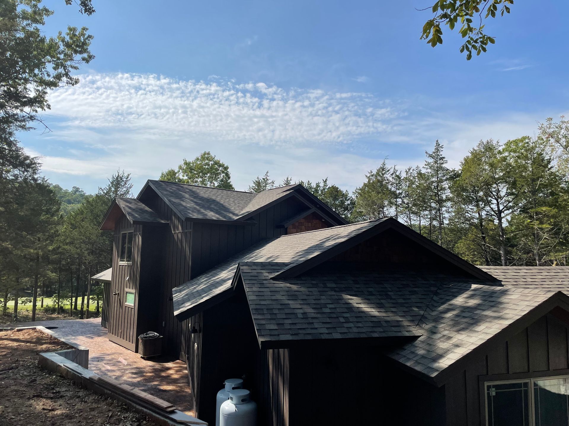 Dark wooden cabins with steep roofs in a sunny wooded setting under a blue sky.