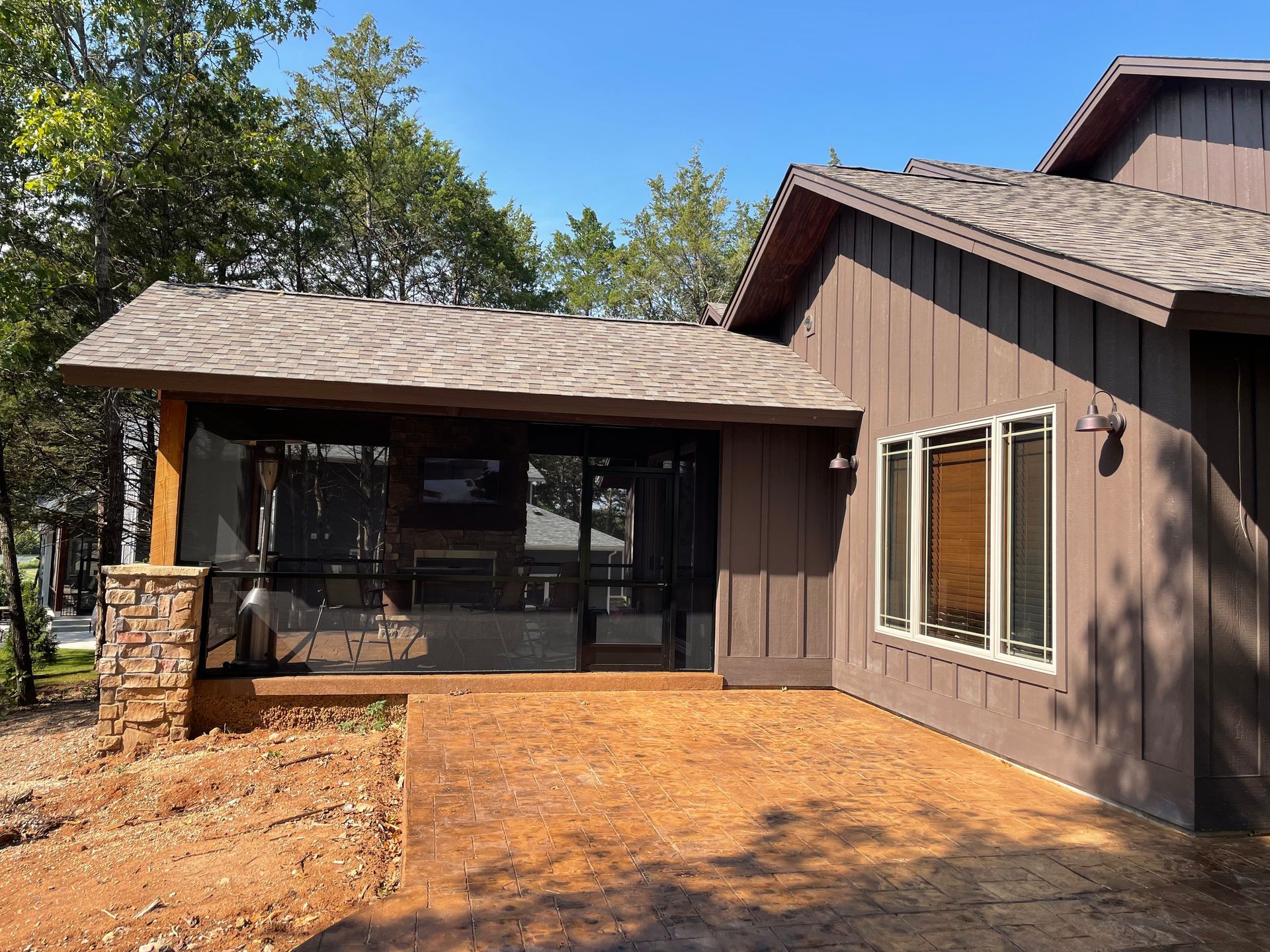 Brown house exterior with screened porch, large windows, and a dirt yard under a blue sky