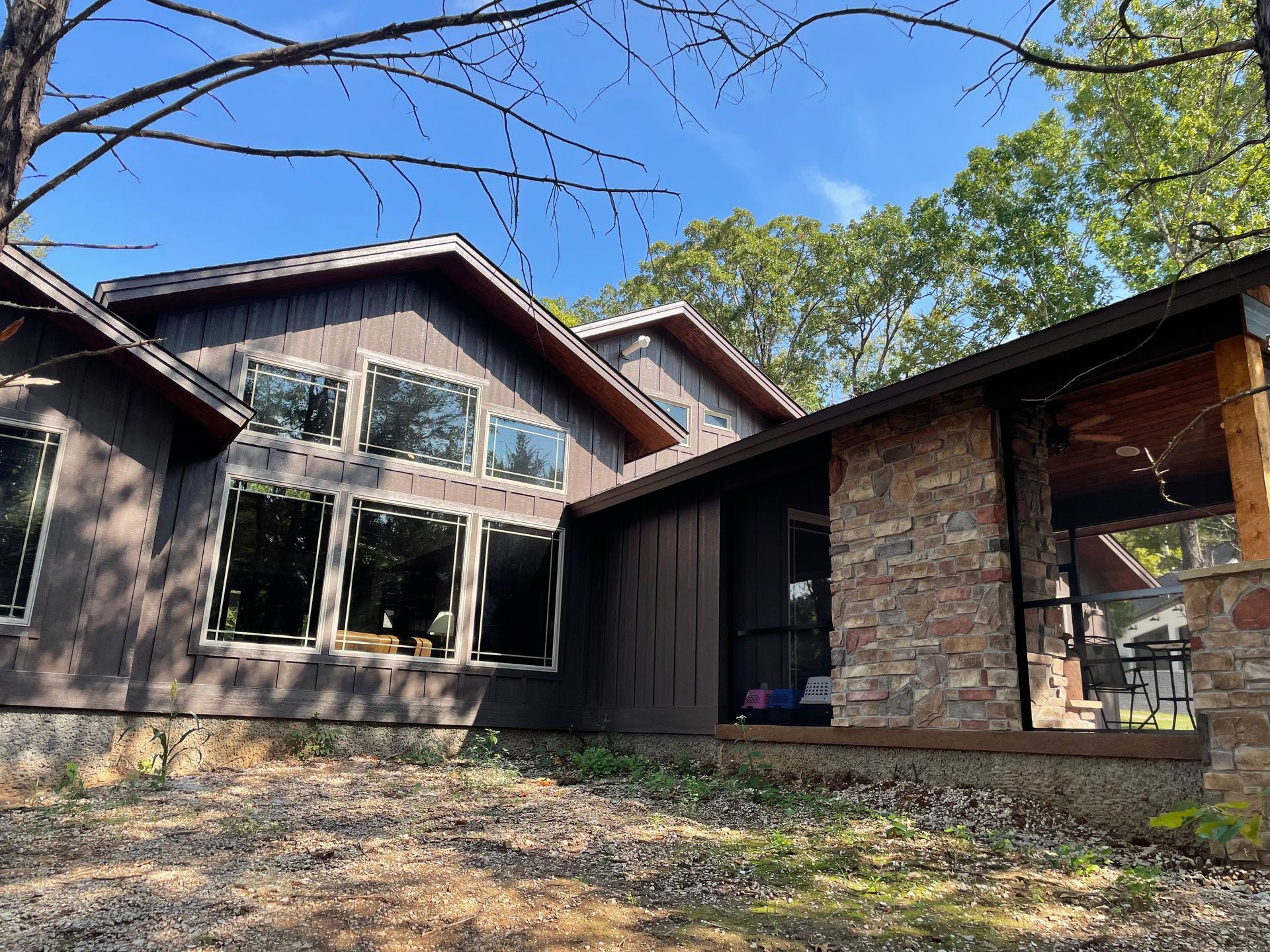 Modern house exterior with stone and wood siding, large windows, and a covered patio under blue sky